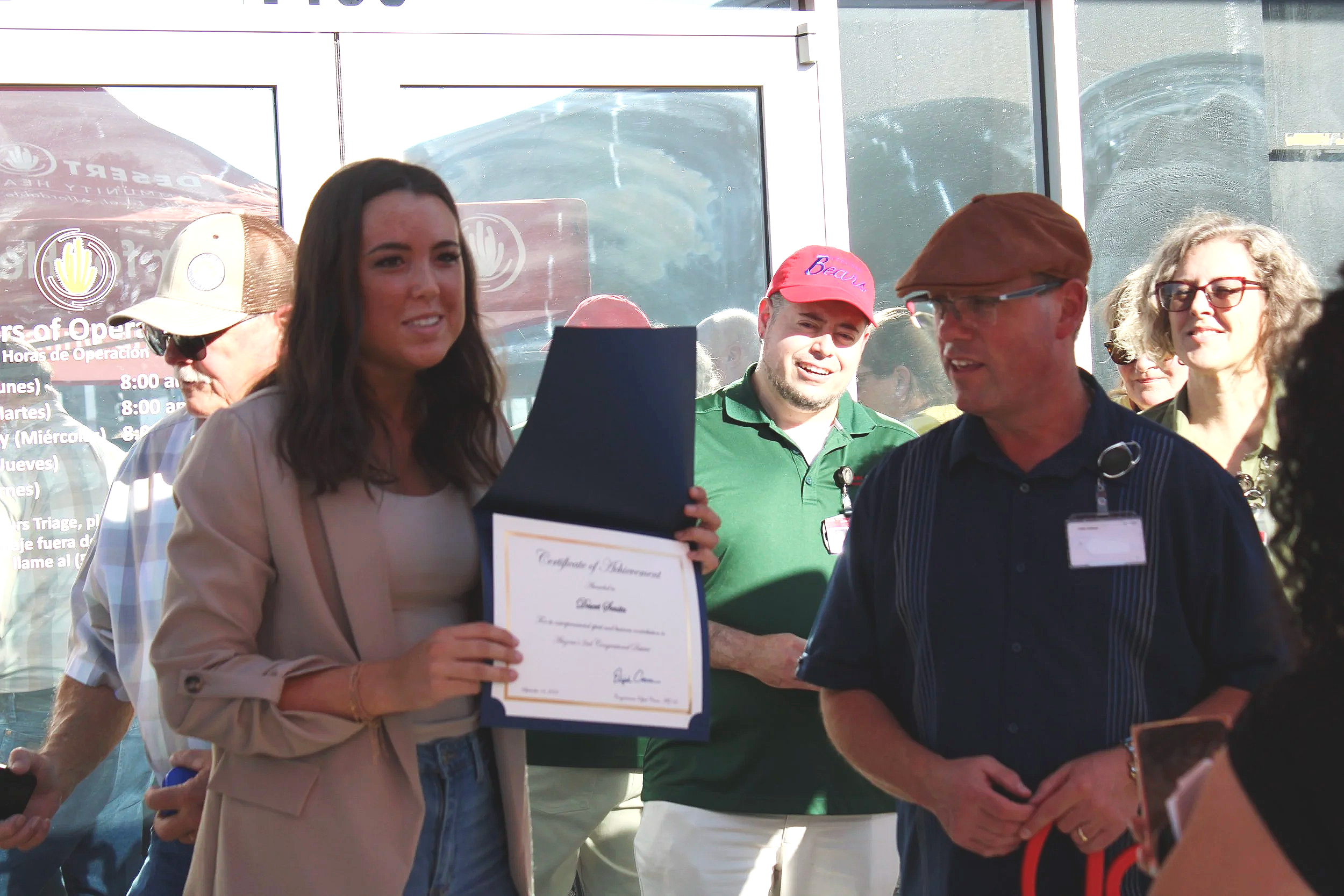 CEO of Desert Senita Community Health Center receiving a Congressional award during the grand opening of Coolidge Clinic, surrounded by people and sunlight. Coolidge, Arizona