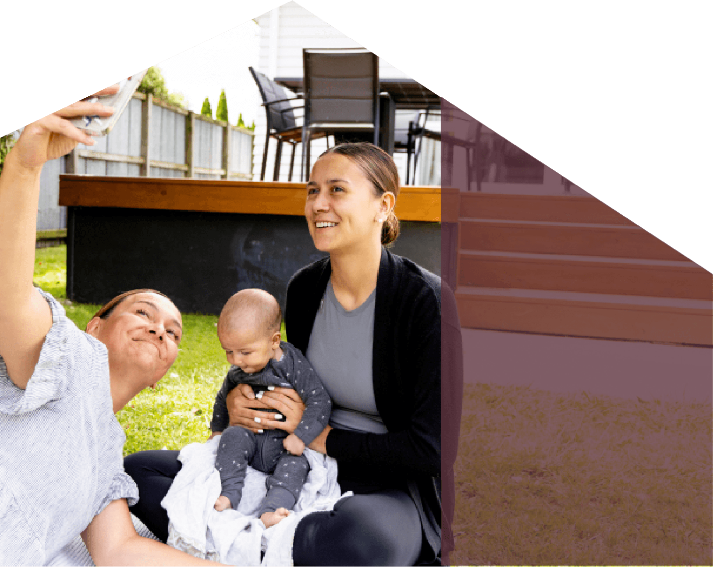A woman and a man with a baby taking a selfie outdoors in their yard, smiling and posing for the photo.