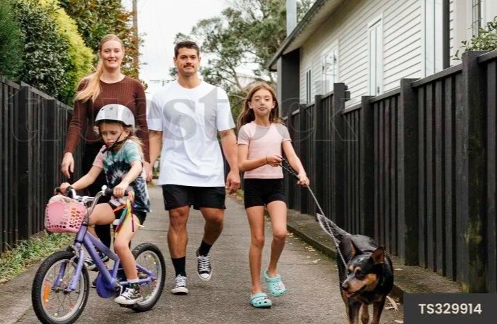 A family of four walking on a sidewalk. The mother, father, and two daughters, one riding a bicycle and the other walking a dog.