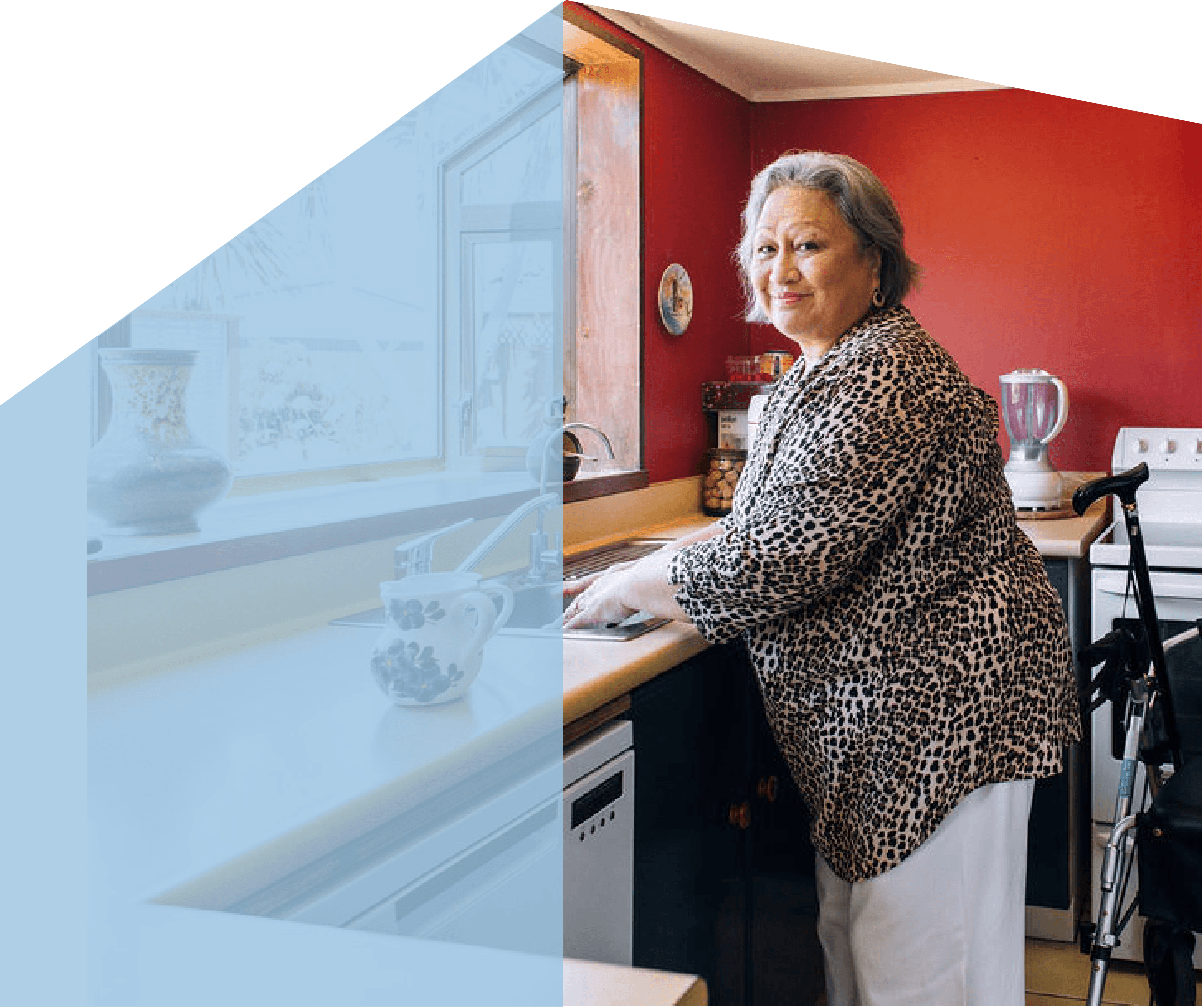 An elderly woman in a leopard-print blouse washing dishes in a kitchen with red walls and a small window.