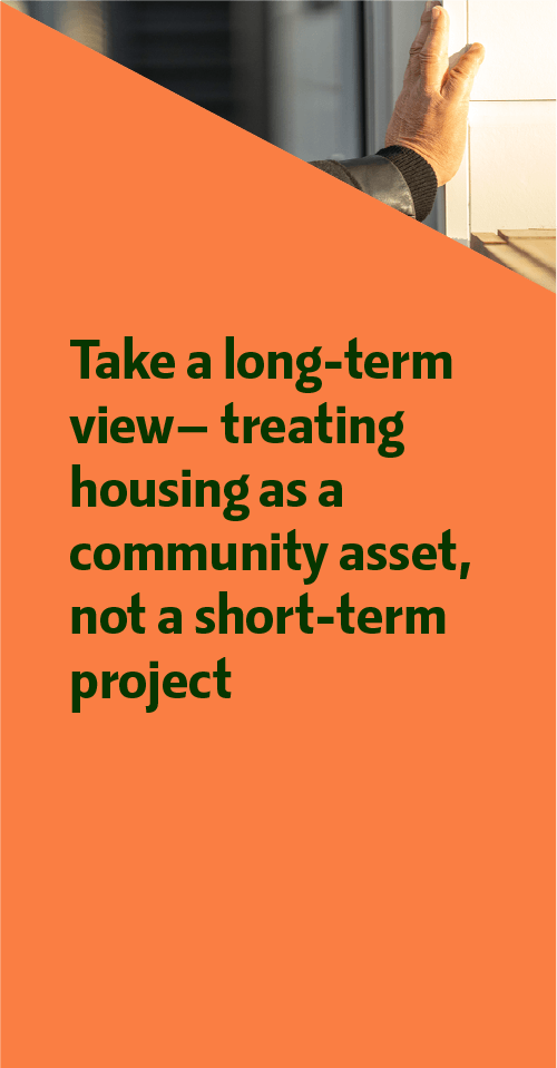 Close-up of a hand resting on a building exterior with a sign that reads, "Take a long-term view--treating housing as a community asset, not a short-term project."