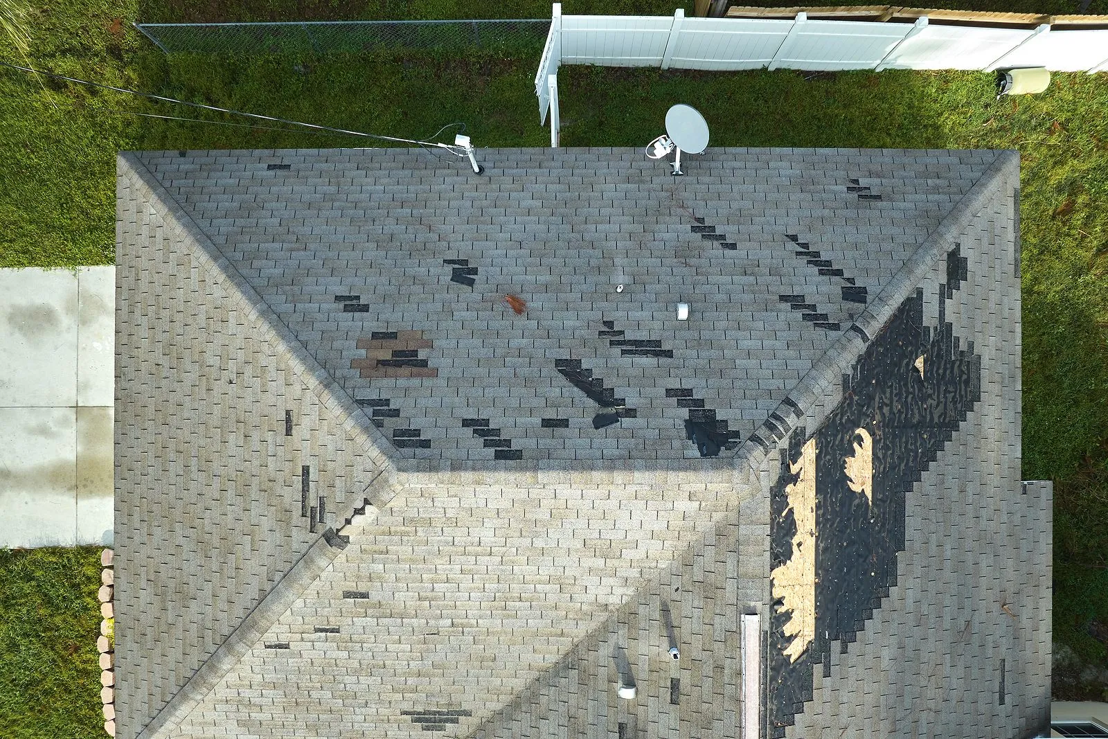 Aerial view of house roof with damaged shingles missing in areas and a satellite dish.