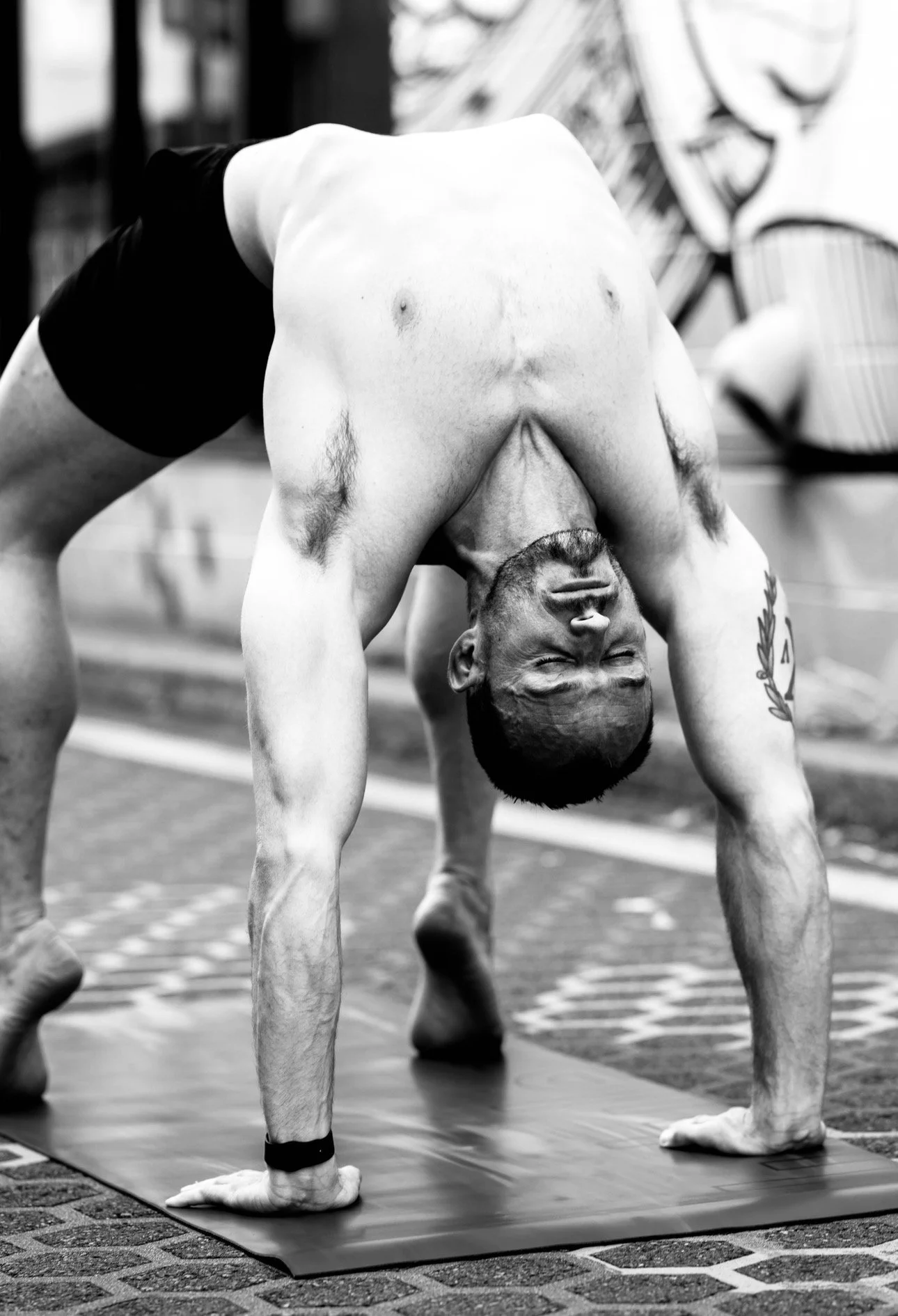 A shirtless man with tattoos practicing yoga in a downward dog pose on a mat indoors.