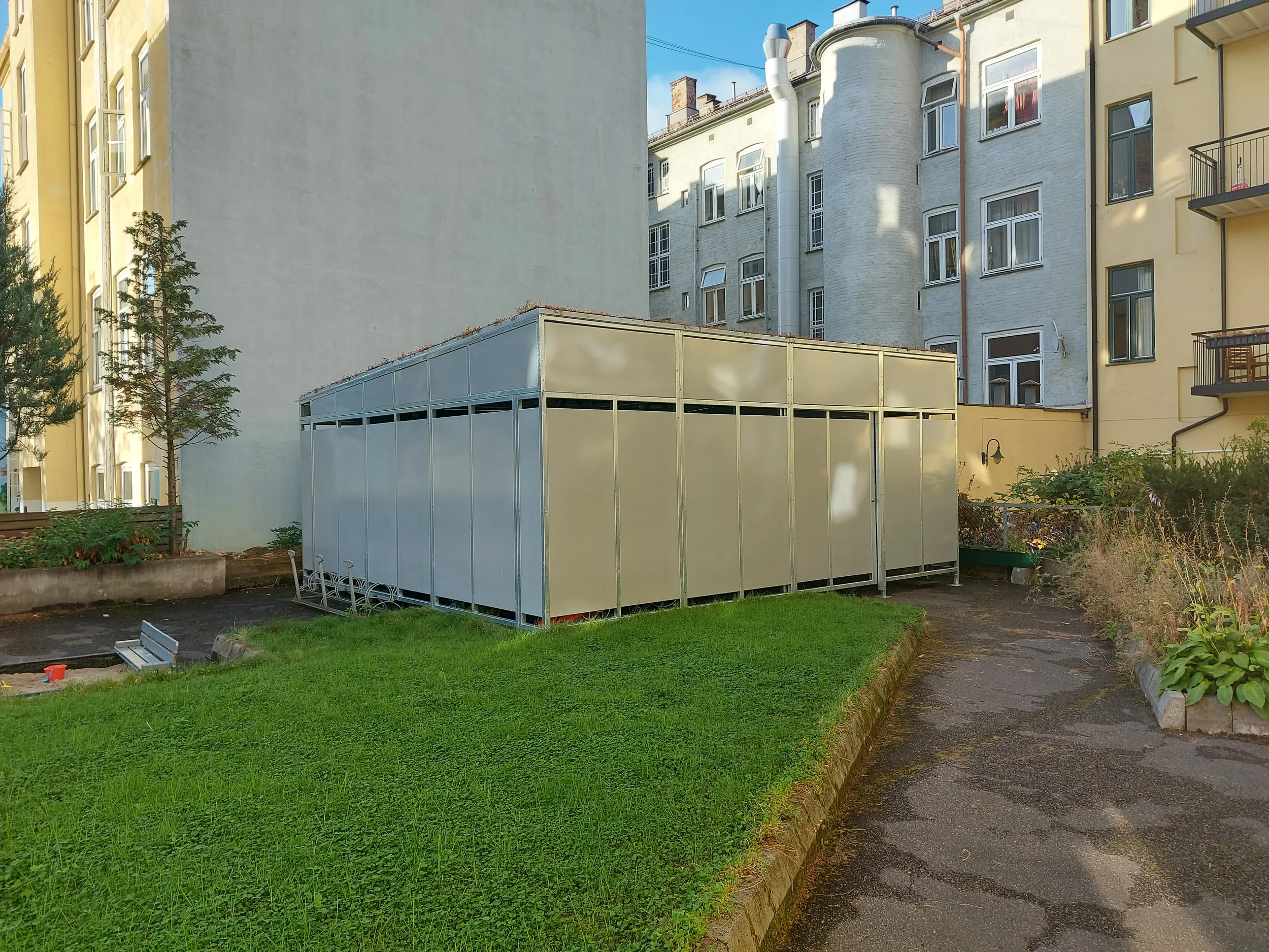 stort sykkelskur i bakgård med skyvedør og sedumtak