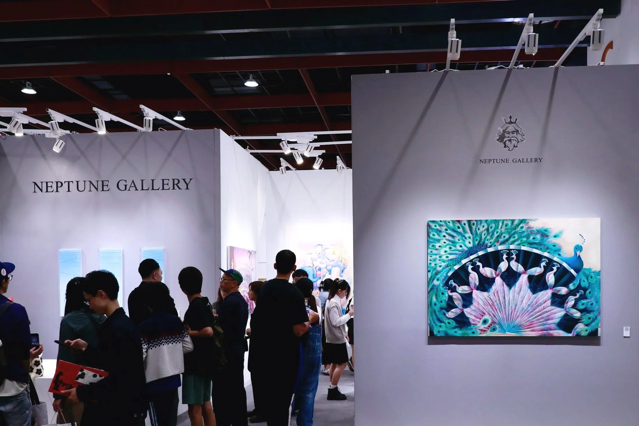 People viewing artwork at Neptune Gallery art exhibition with white walls, spotlighting colorful peacock painting and others in background.