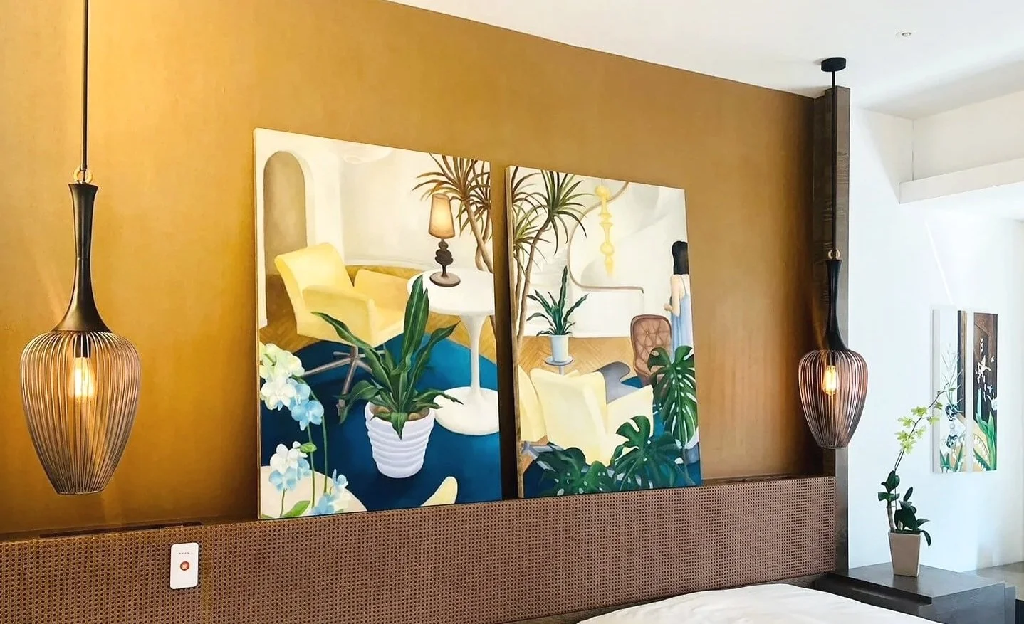 Decorative interior scene with two paintings of botanical and living room scenes, pendant lights, and potted plants.