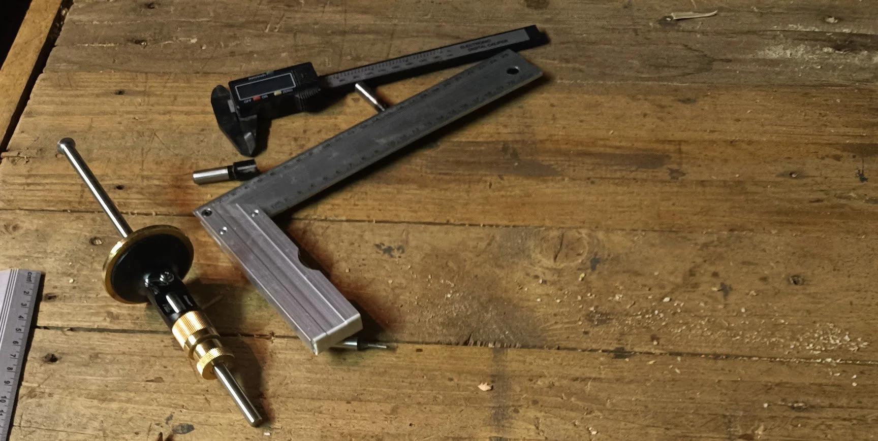 Outils de menuiserie, inclut un cube de rail, un compas à réglage d'angle et deux règles métalliques, posés sur une surface en bois.