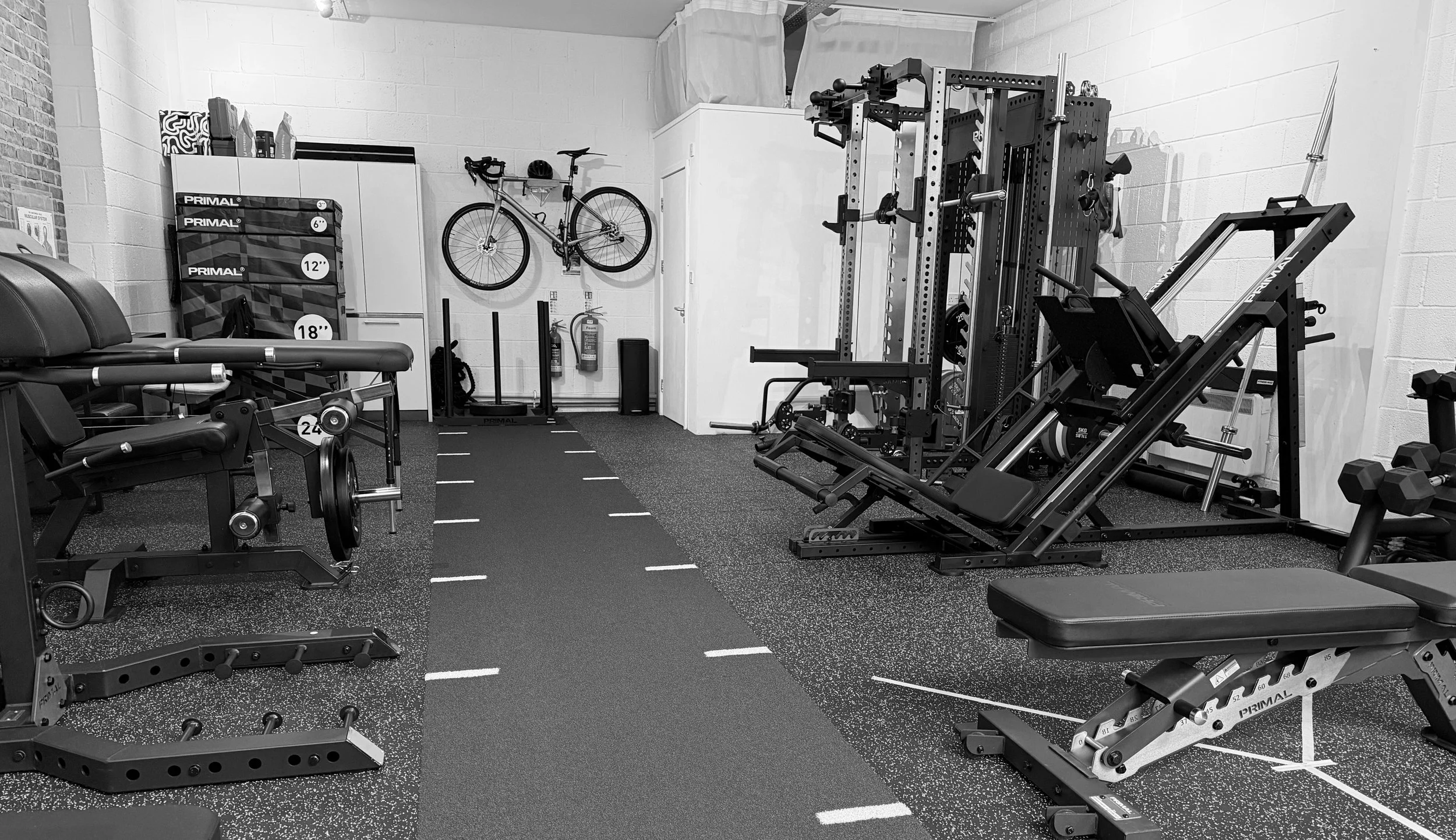 Empty gym with workout machines, weights, a wall-mounted bike, and fitness equipment in black and white.