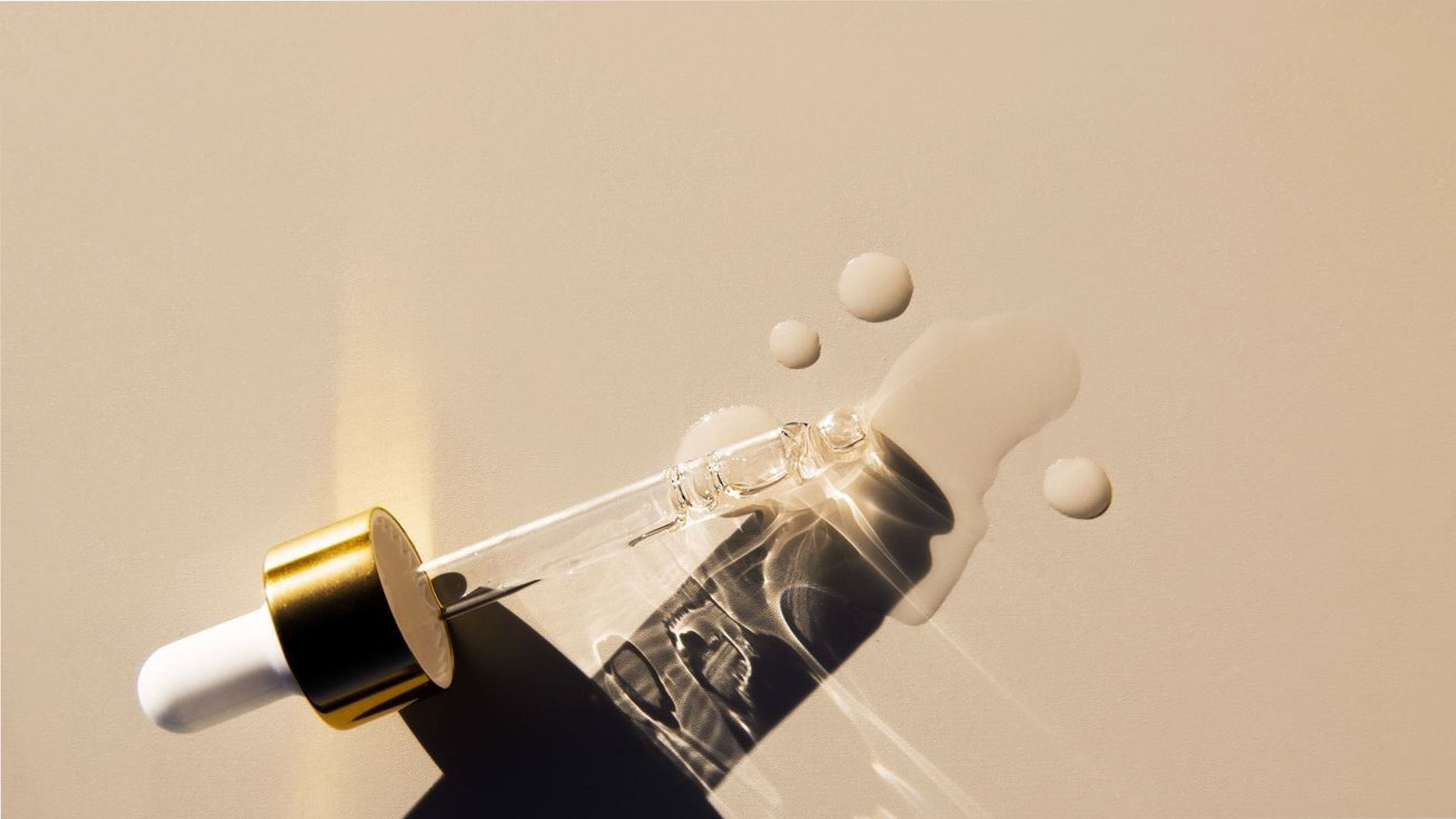 A glass dropper with a white and gold cap dispensing a clear liquid, creating splashes and bubbles against a light background.