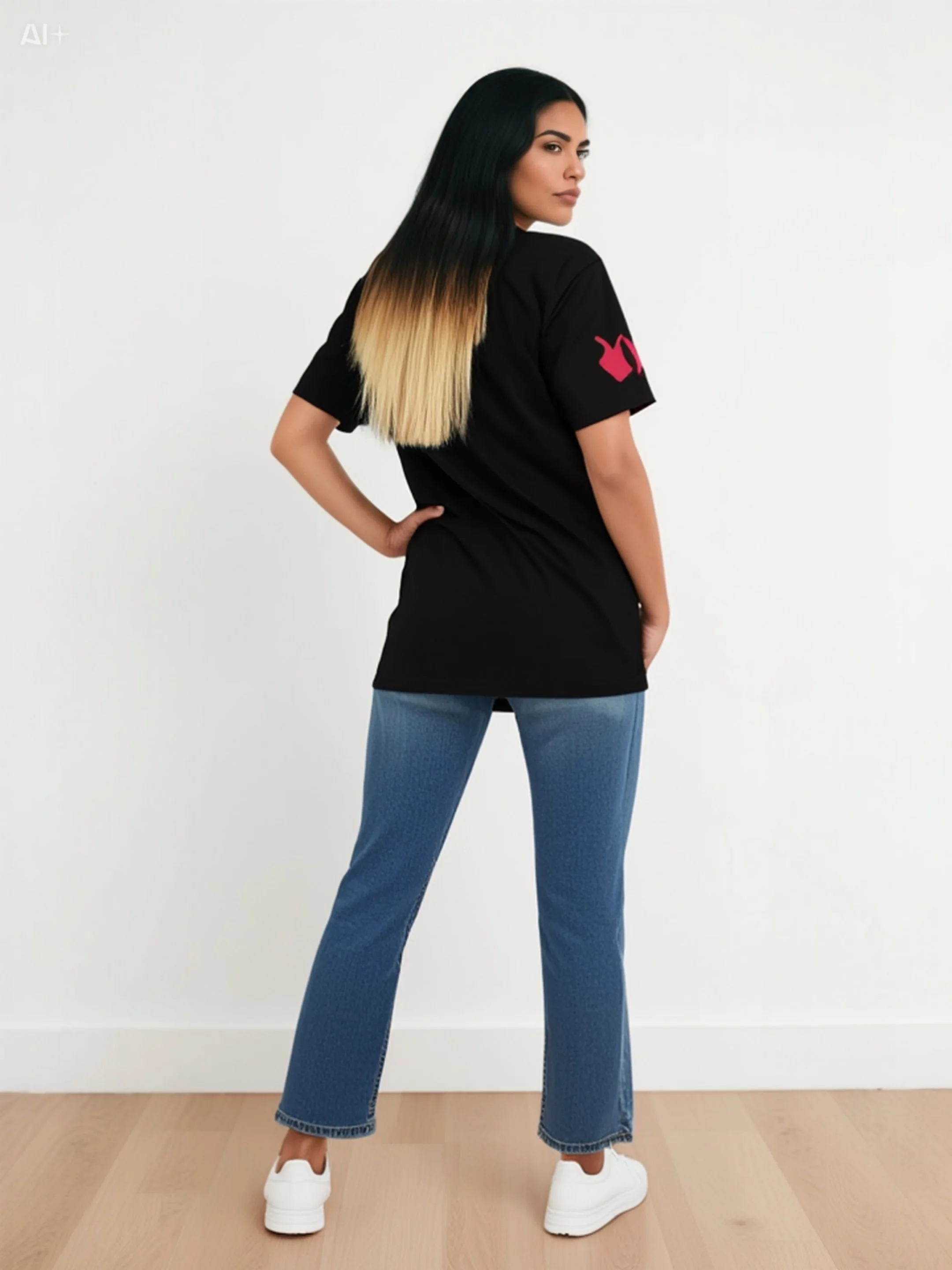 A woman standing with her back to the camera, head turned to the side, wearing a black t-shirt with a pink lightning bolt on the sleeve, blue jeans, and white sneakers, against a plain white wall.