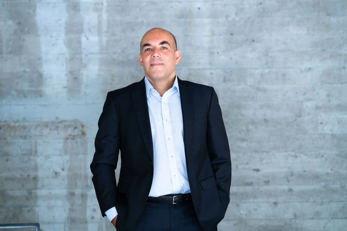 Ein Mann in Businesskleidung steht an einer weißen Wand in einem modernen Raum.