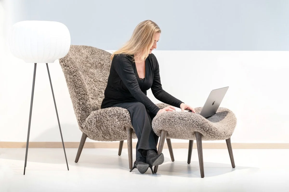 Frau sitzt auf einem bequemen Sessel mit Fußhocker, arbeitet an einem Laptop, in einem modern eingerichteten Raum.