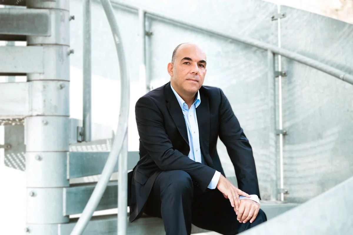 Ein Mann in einem schwarzen Anzug sitzt auf einer Treppe aus Metall in einem modernen Gebäude