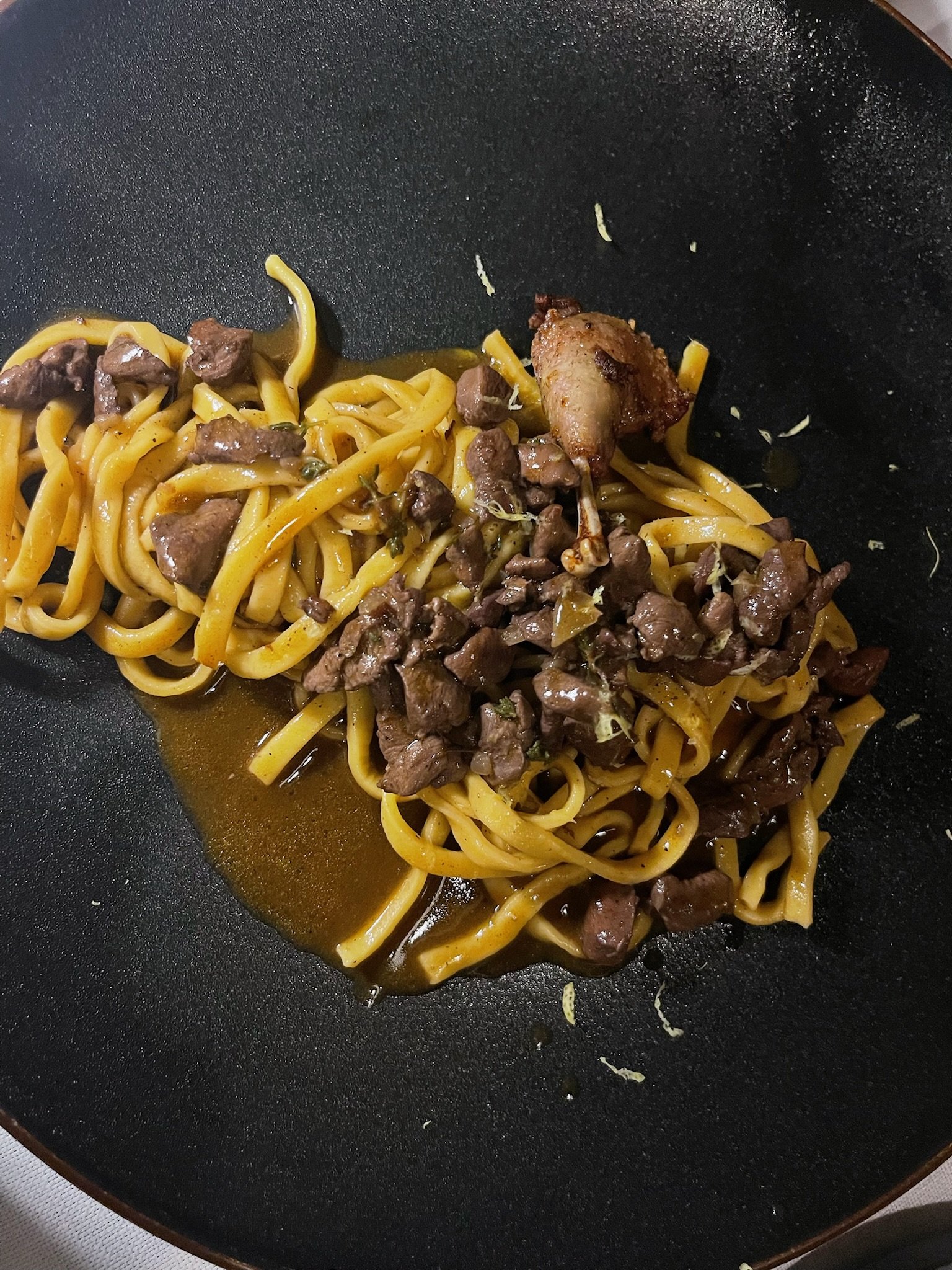 Stir-fried noodles with chunks of beef and a piece of chicken wing in a black wok.