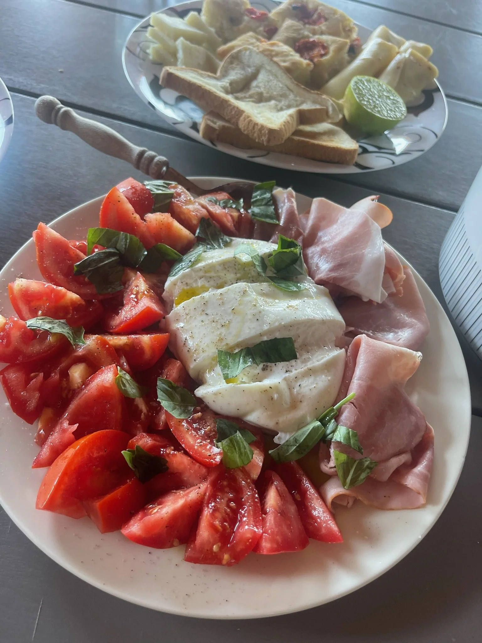 Plate of sliced tomatoes, fresh basil, a poached egg, and slices of ham.