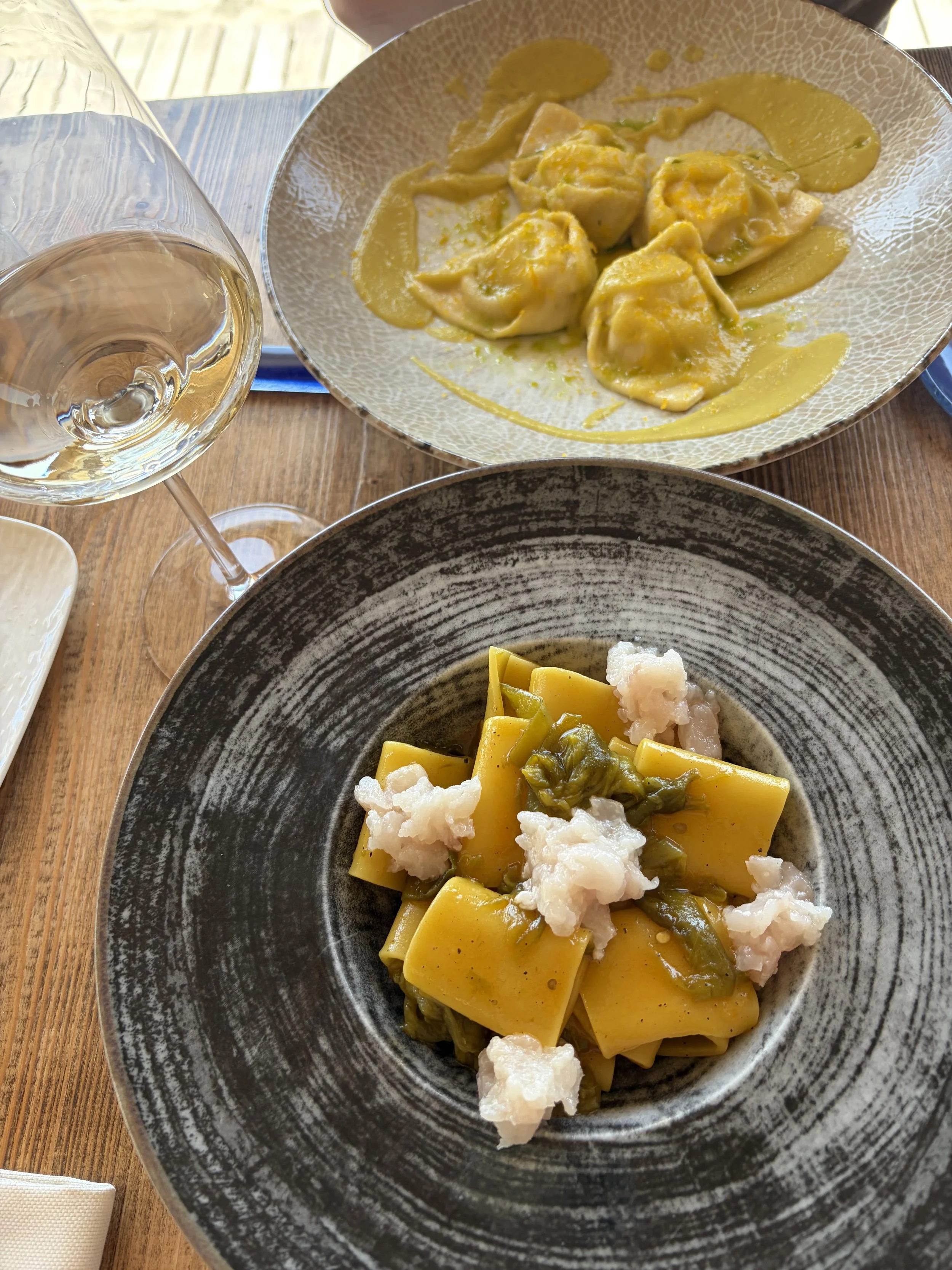 Plate of yellow ravioli with white seafood pieces and green vegetables, served on a black and gray textured bowl.