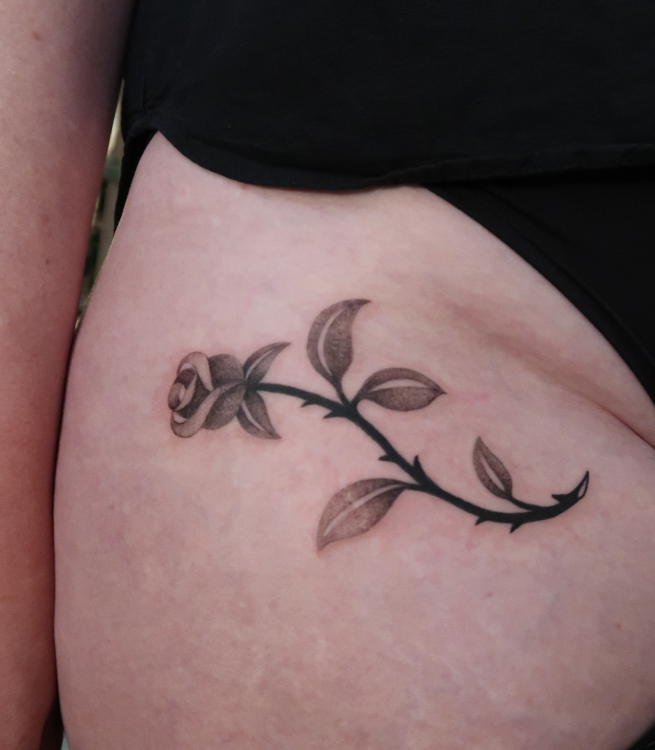 A tattoo of a softly shaded rose in black ink, flowing and curving beautifully on the hip.  Done by Wanissa, an experienced tattooer based in Melbourne, Australia.