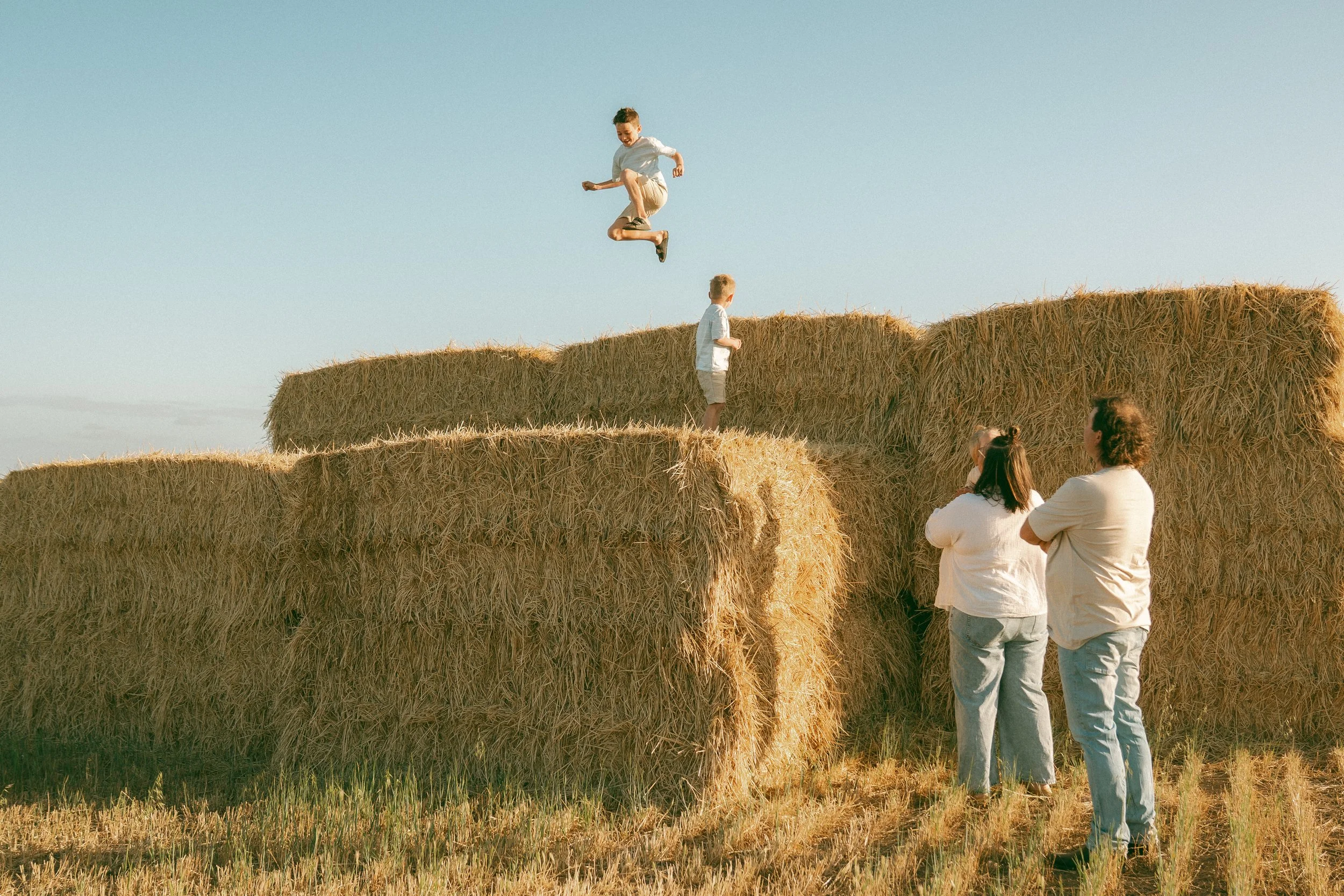Mum dad and 2 kids jumping off hay bales during a farm family photoshoot at streaky bay