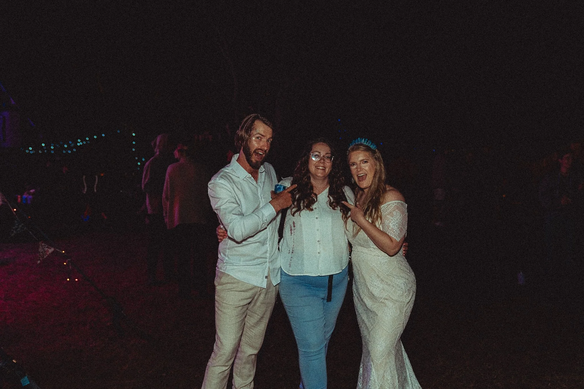 Three friends celebrating at a nighttime event, with two women and a man in the center smiling, laughing, and making playful gestures.