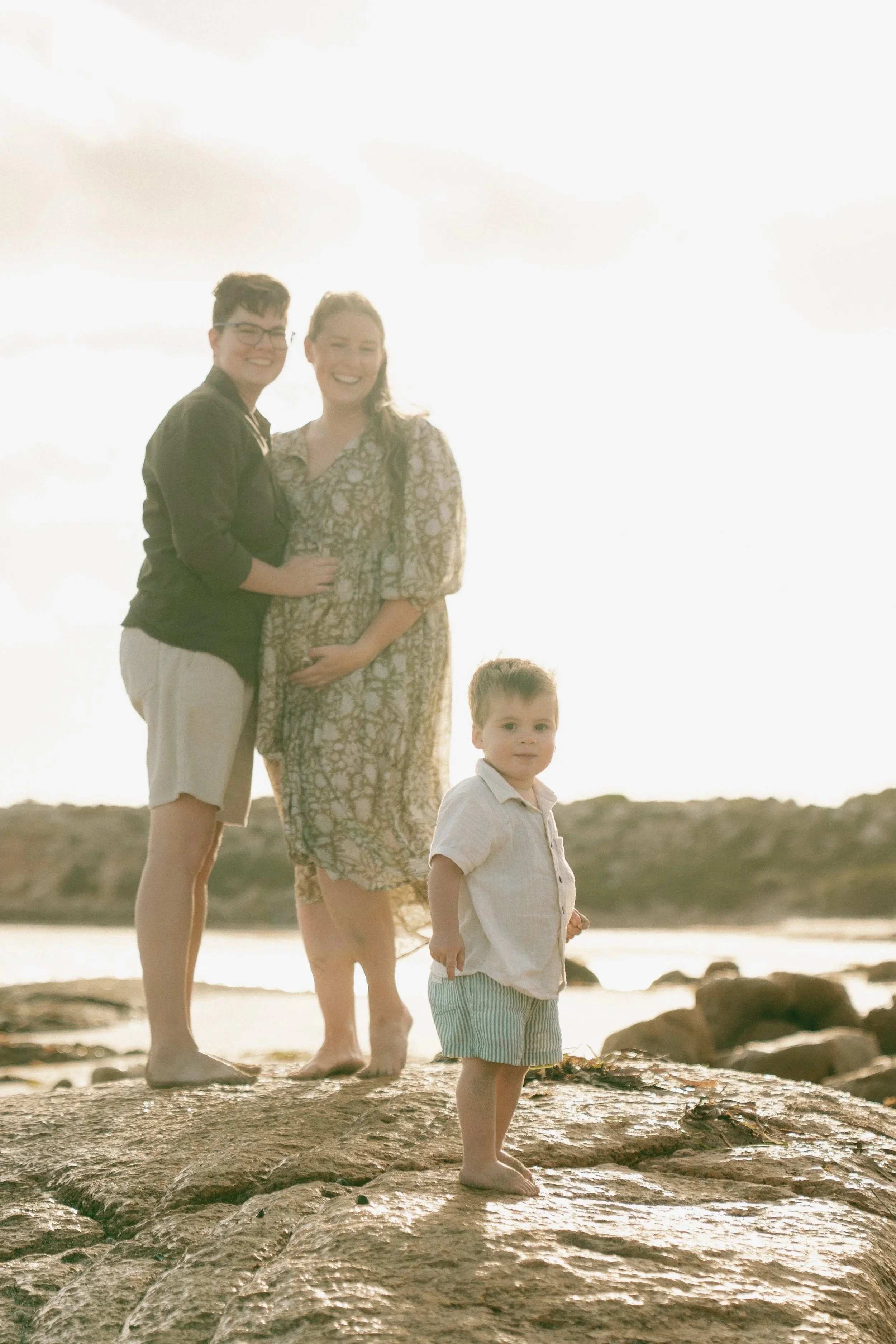 Family of three standing on a rocky beach at sunset, with water and a hill in the background in ceduna Eyre Peninsula