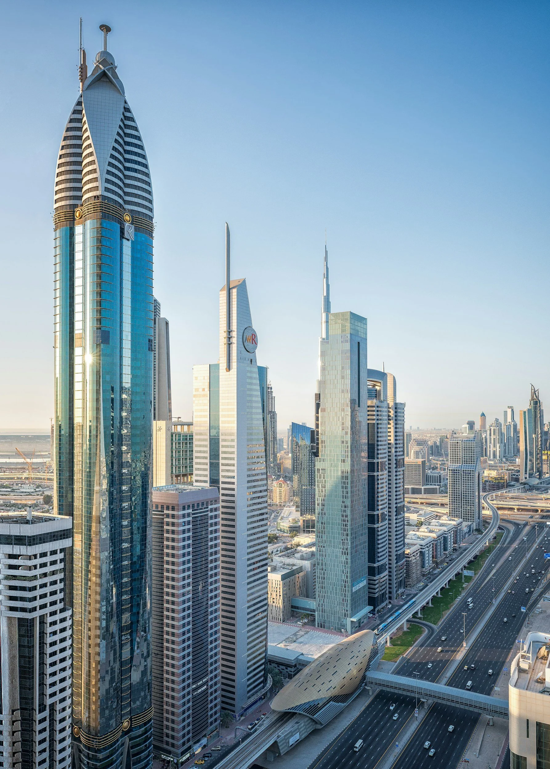 Skyline of Dubai with tall modern skyscrapers and highways, under a clear blue sky.