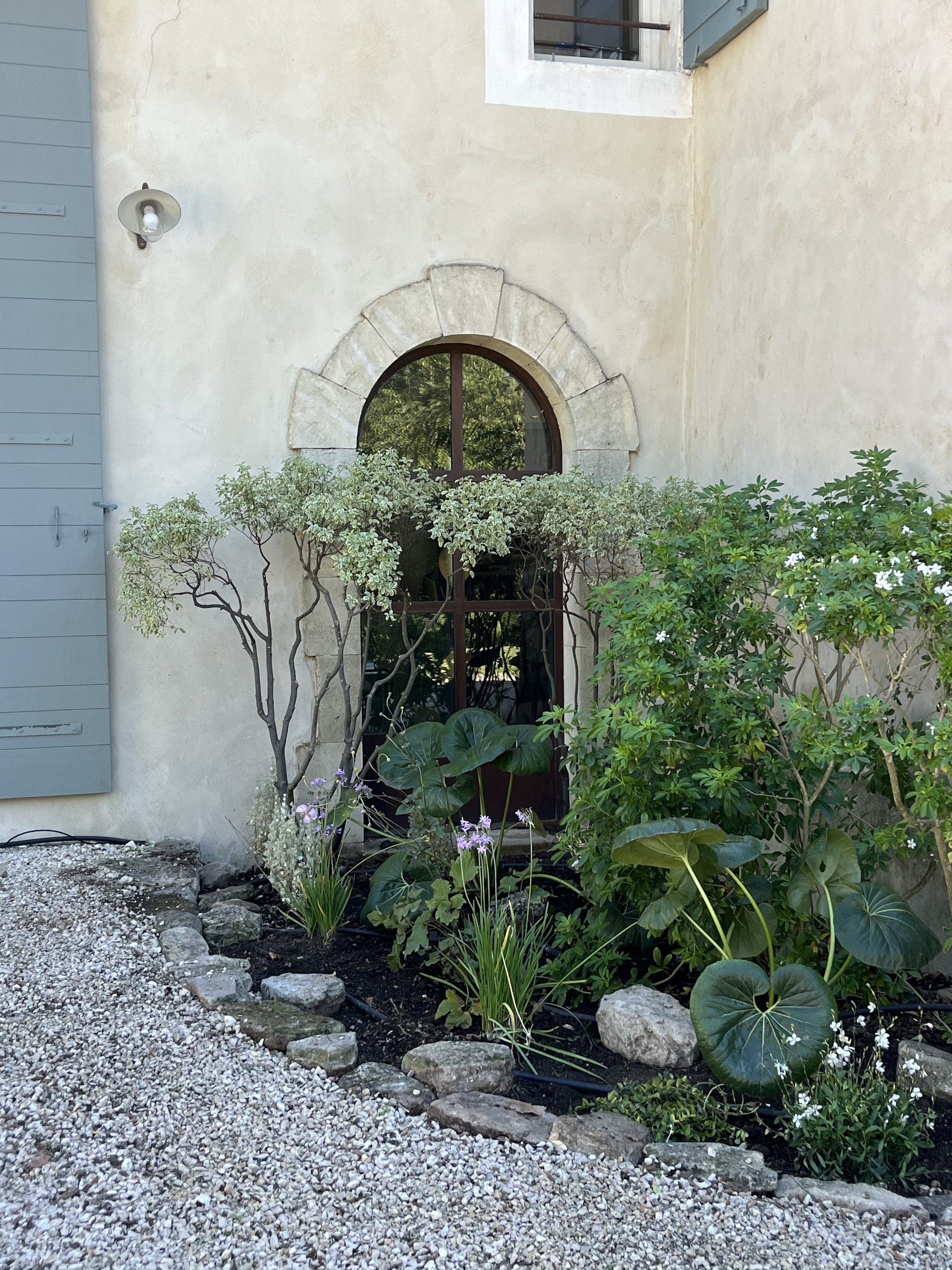 Front view of a house with a semi-circular window surrounded by stonework, plants, and shrubs in a landscaped garden bed.