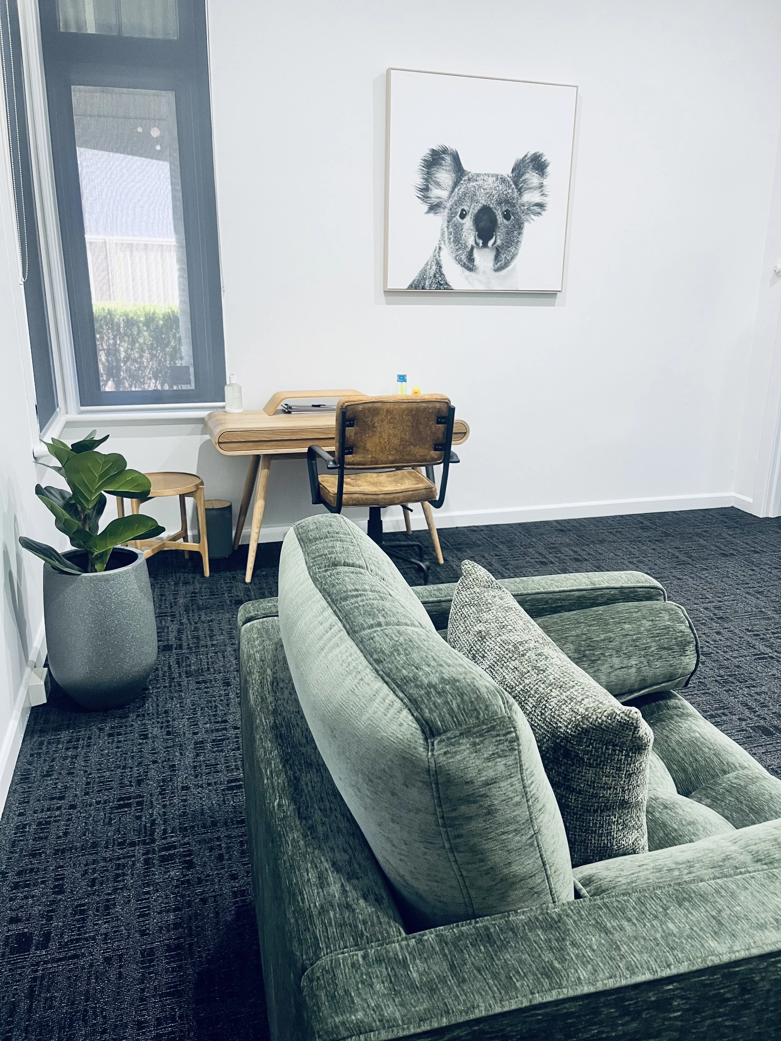 Craig Salisbury's consult room at Combined Minds Psychology in Perth featuring a soft green couch, plant and cute wall art of a koala