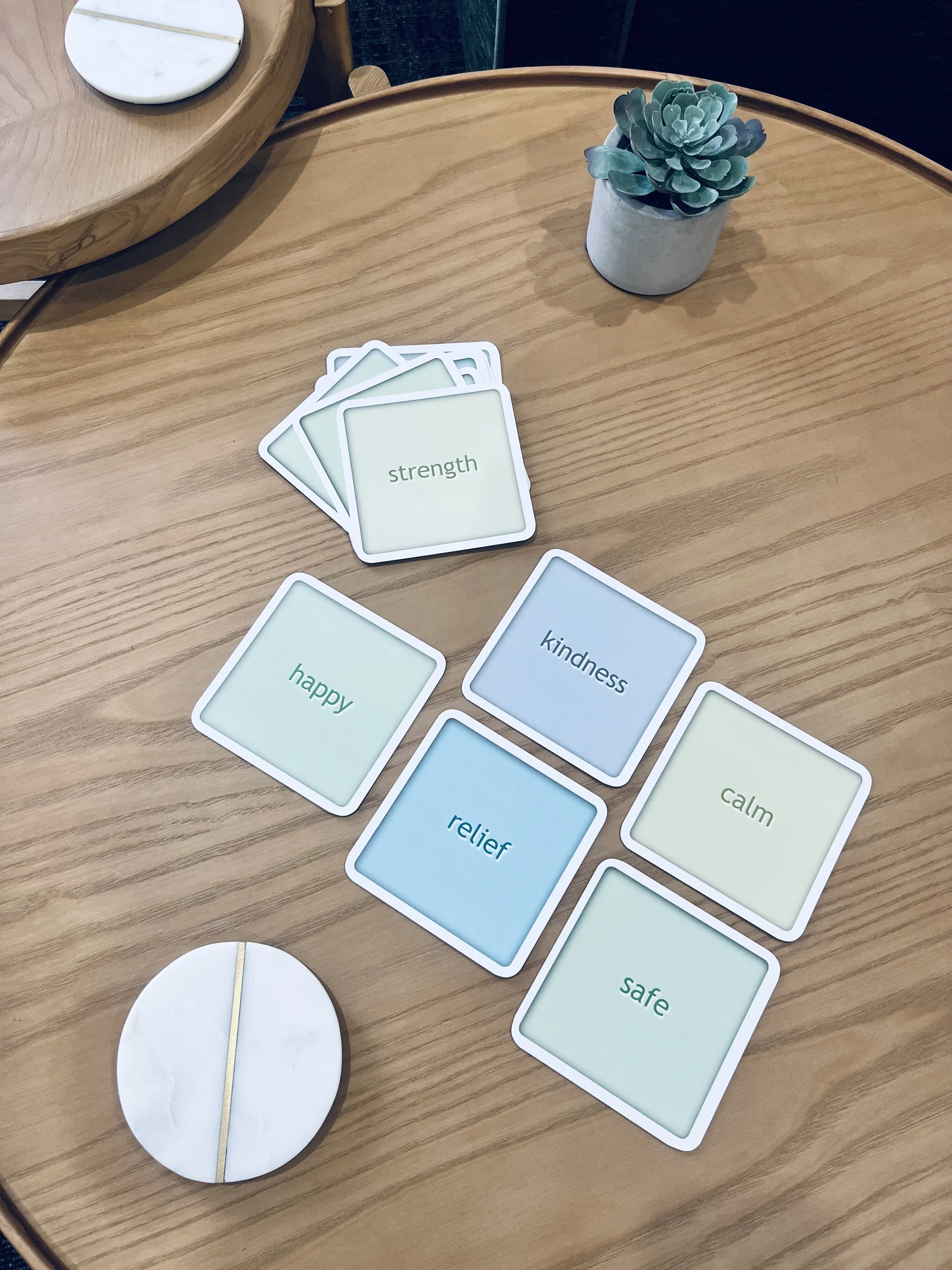 A set of flash cards on a coffee table being used in a psychology session with a teenager. The cards show the words strength, happy, kindness, relief, calm and safe