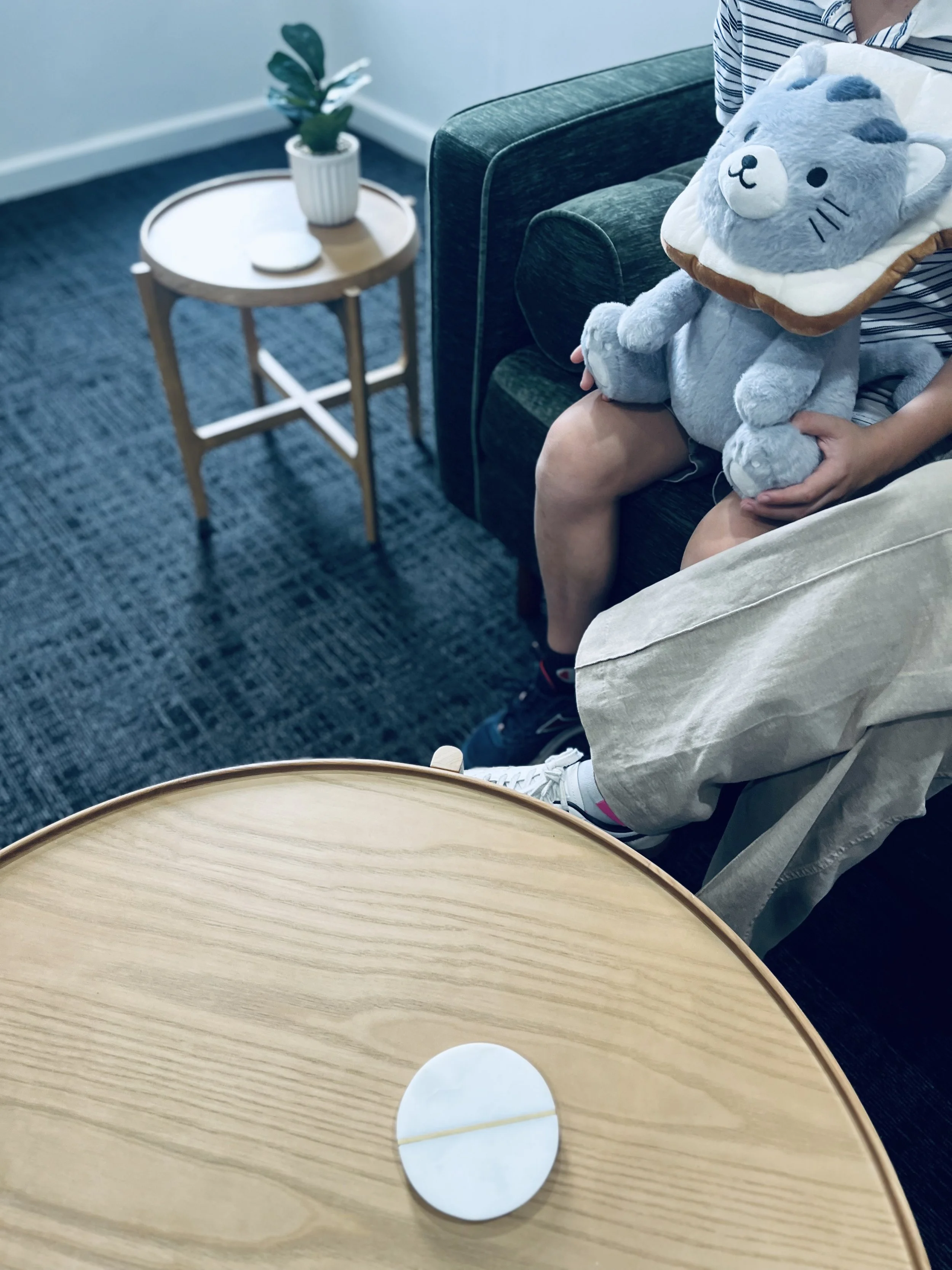 Child and parent sitting on couch together attending therapy with their psychologist. Child is holding a plush toy and the parent sits close to them