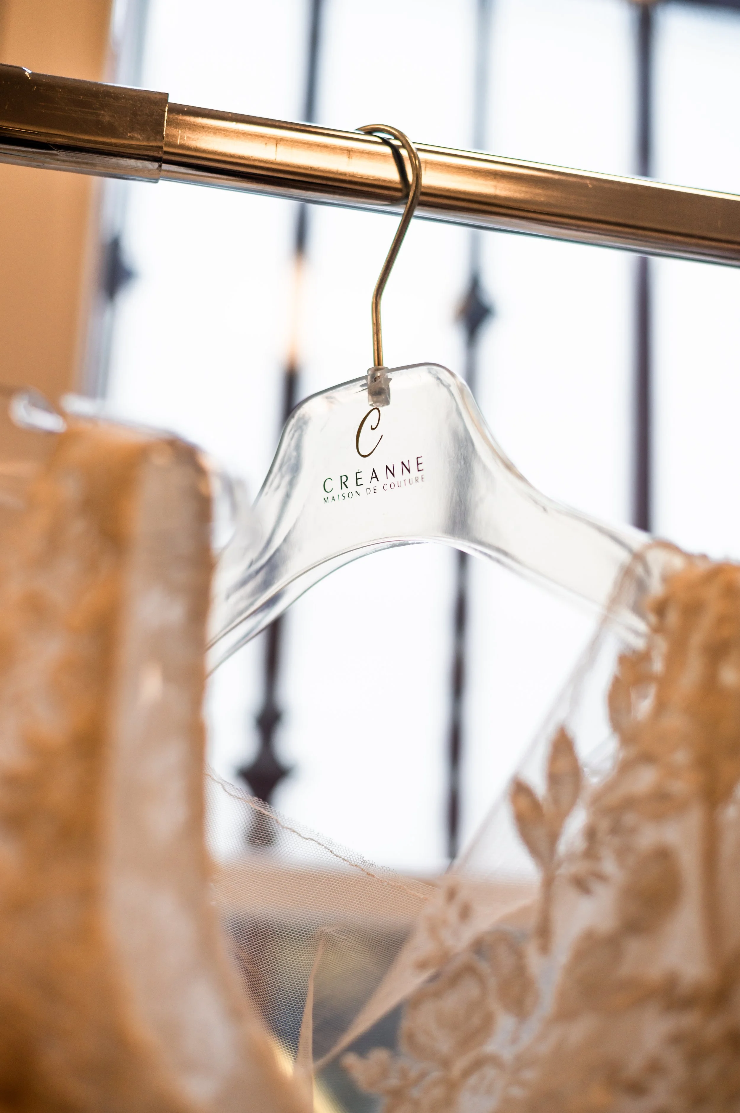 Vêtements de couture suspendus sur un portant en métal en intérieur, marque 'C Créanne Maison de Couture' visible sur un cintre en plastique transparent.