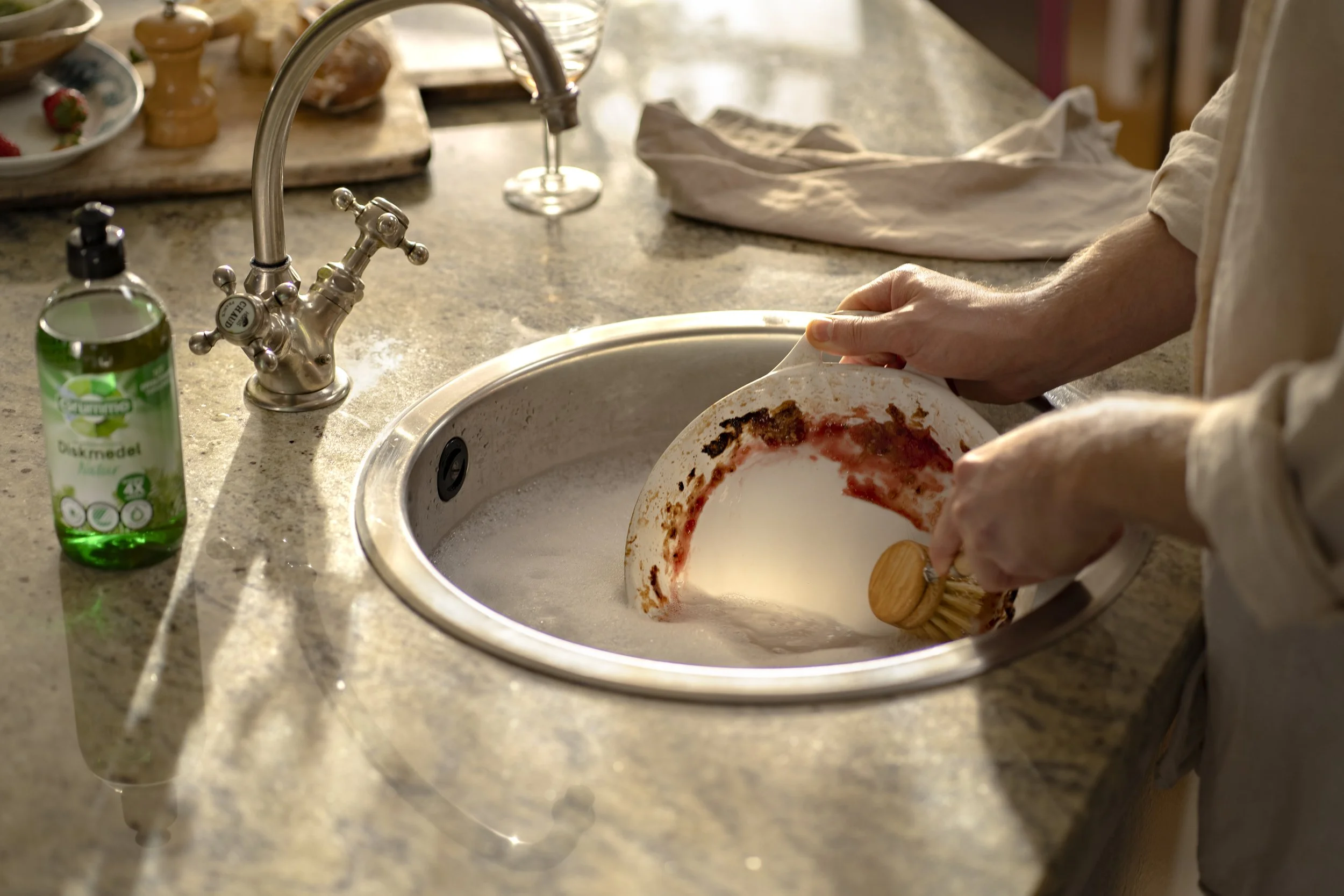 Person washing a dirty plate in a kitchen sink with soap and water.