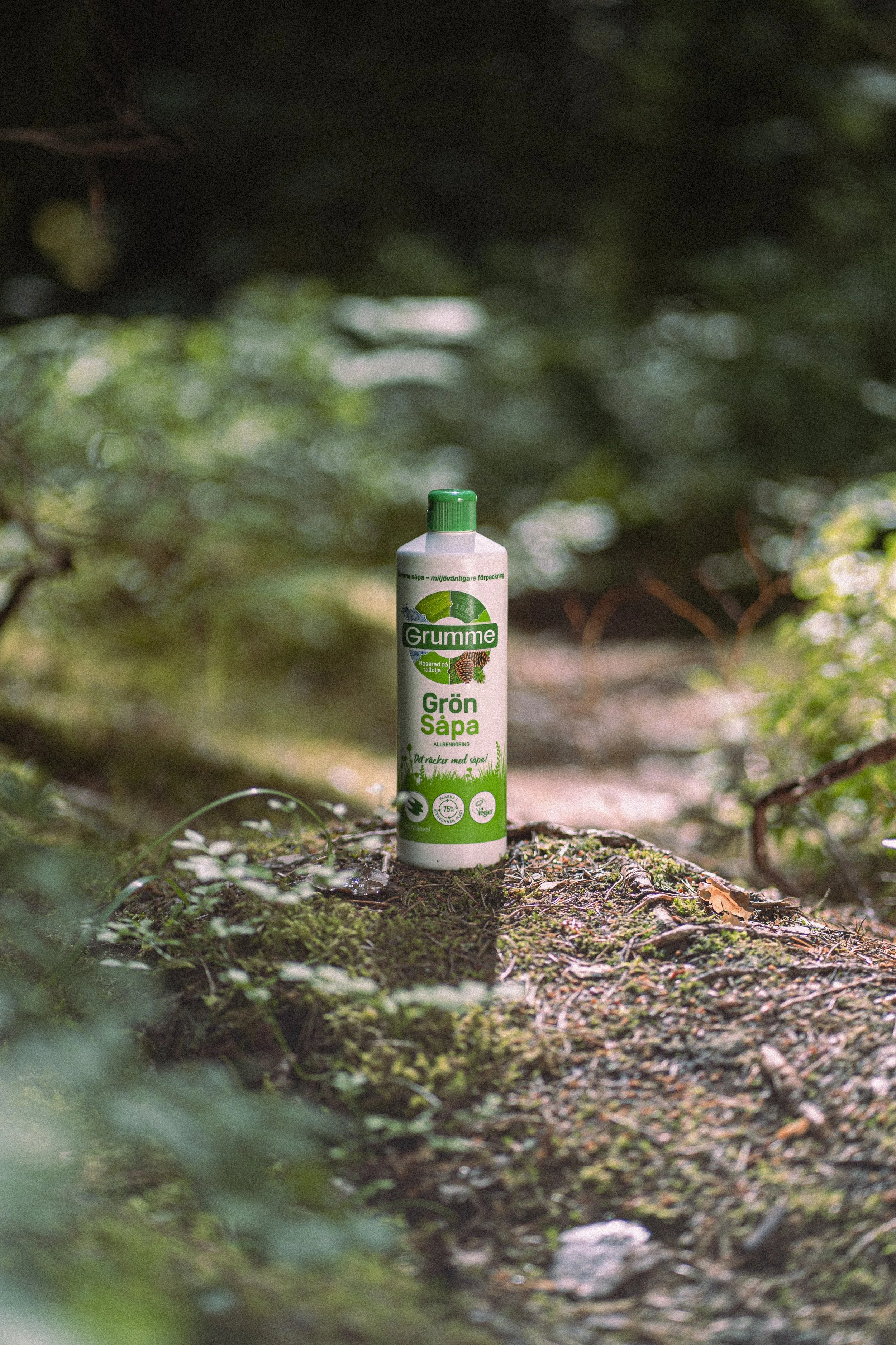 Spray bottle of Grumme Green Soap standing on a mossy log in a forest.