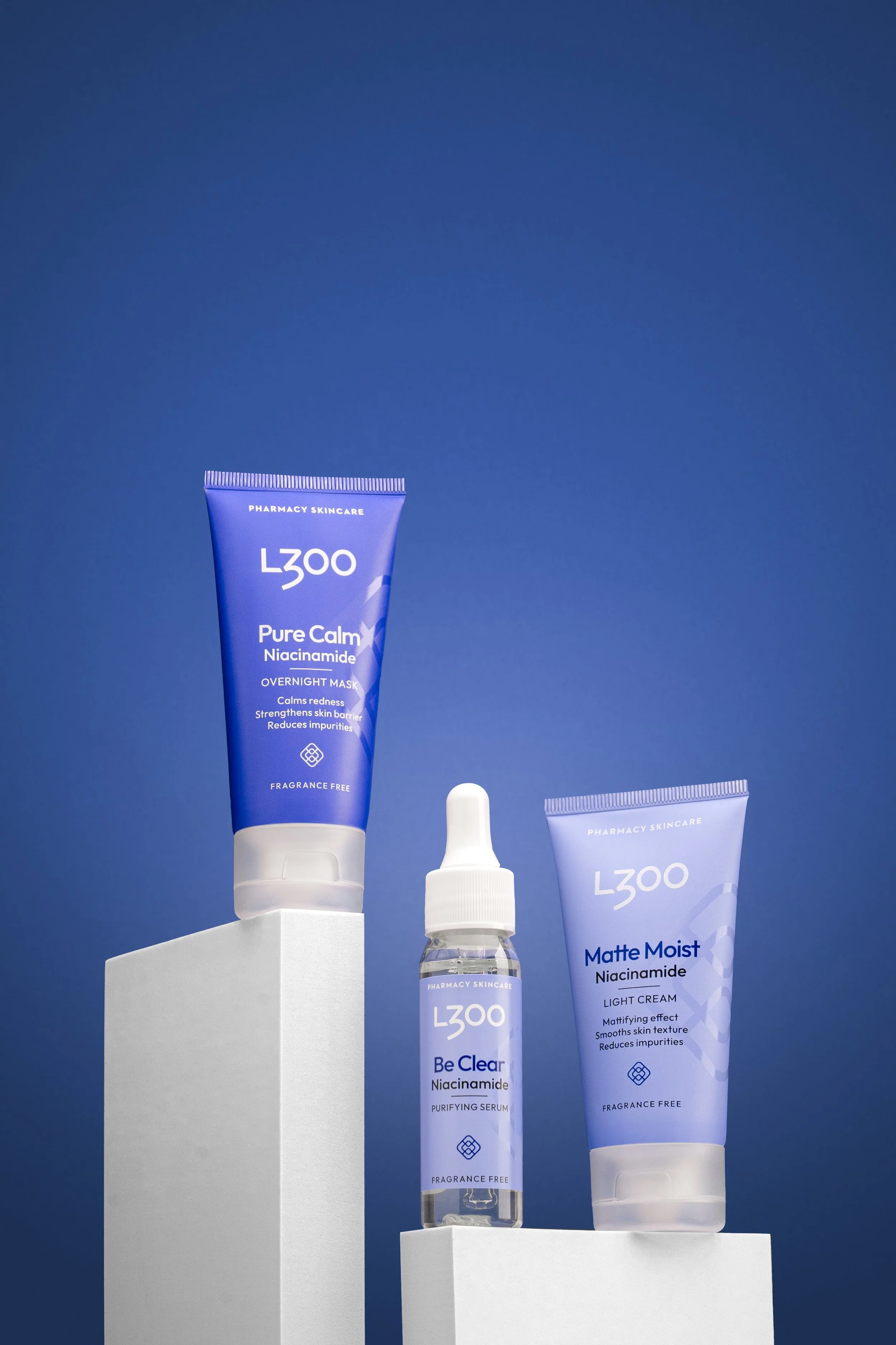 Three skincare products from the LZOO brand against a blue background, including a purple tube labeled 'Pure Calm Niacinamide Overnight Mask,' a clear spray bottle labeled 'Be Clear Niacinamide Purifying Serum,' and a purple tube labeled 'Matte Moist