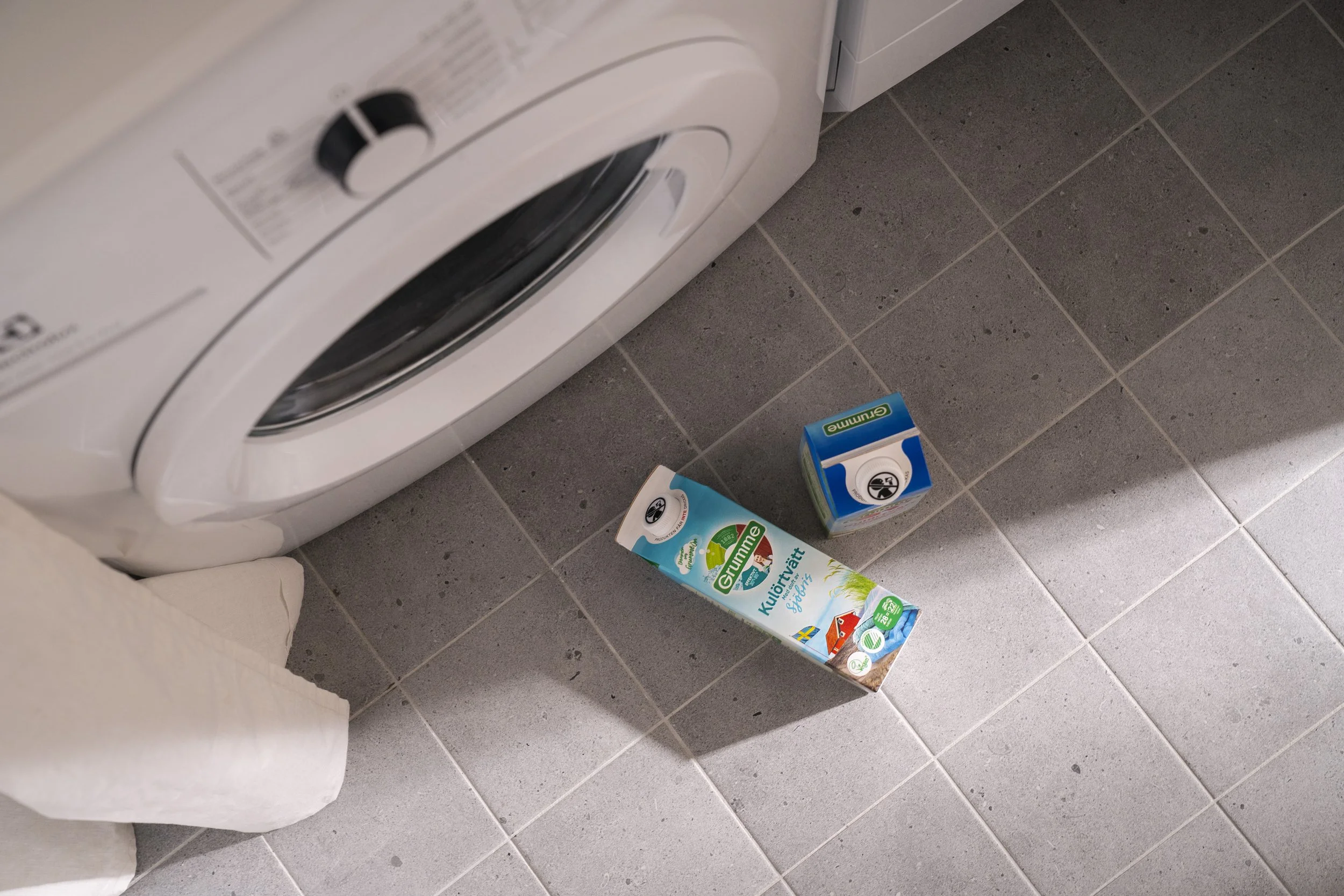 A washing machine in a laundry room with a box of washing powder and a box of fabric softener on tiled floor.