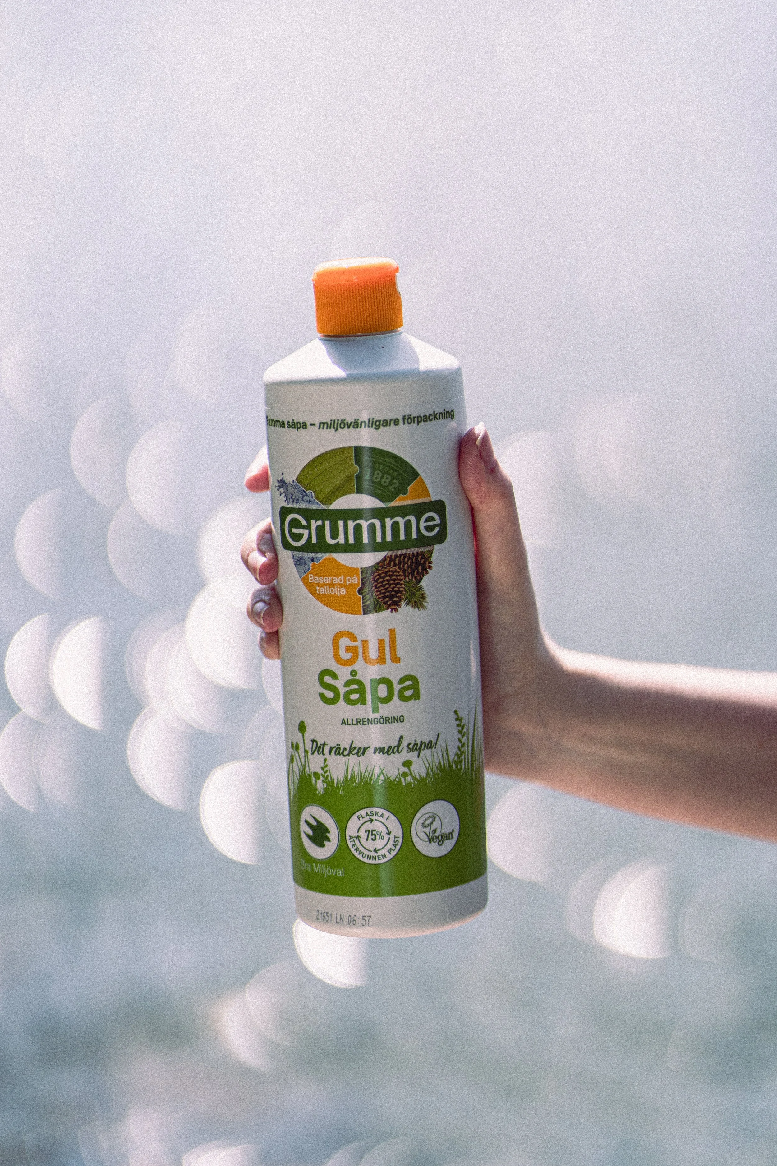 A person's hand holding a bottle of eco-friendly cleaning spray labeled 'Gul Såpa' against a blurred background with circular bokeh lights.