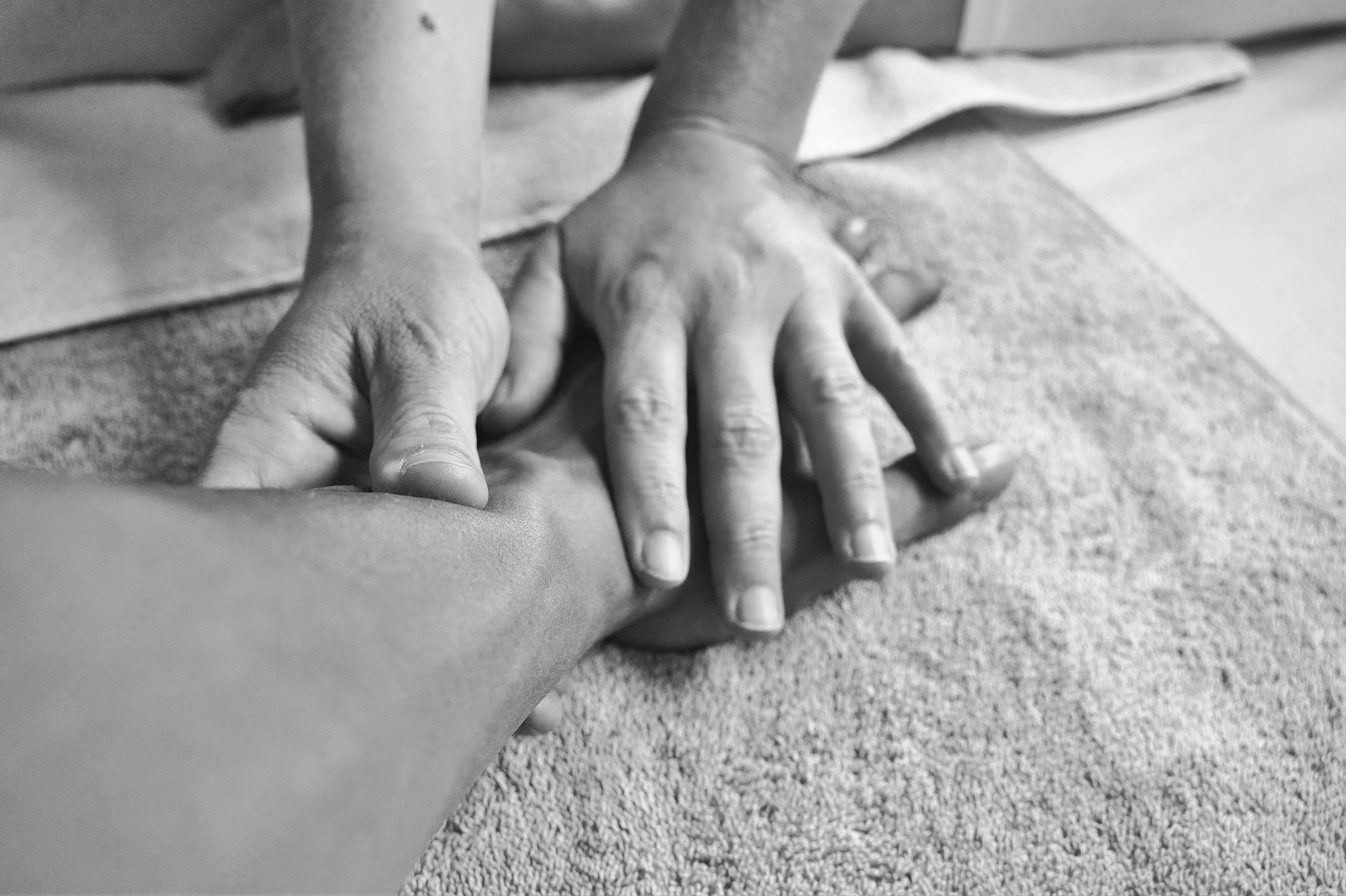 A person is receiving a massage, lying face down on a massage table with a towel under their back. The massage therapist's hands are applying pressure to the person's shoulder blades.