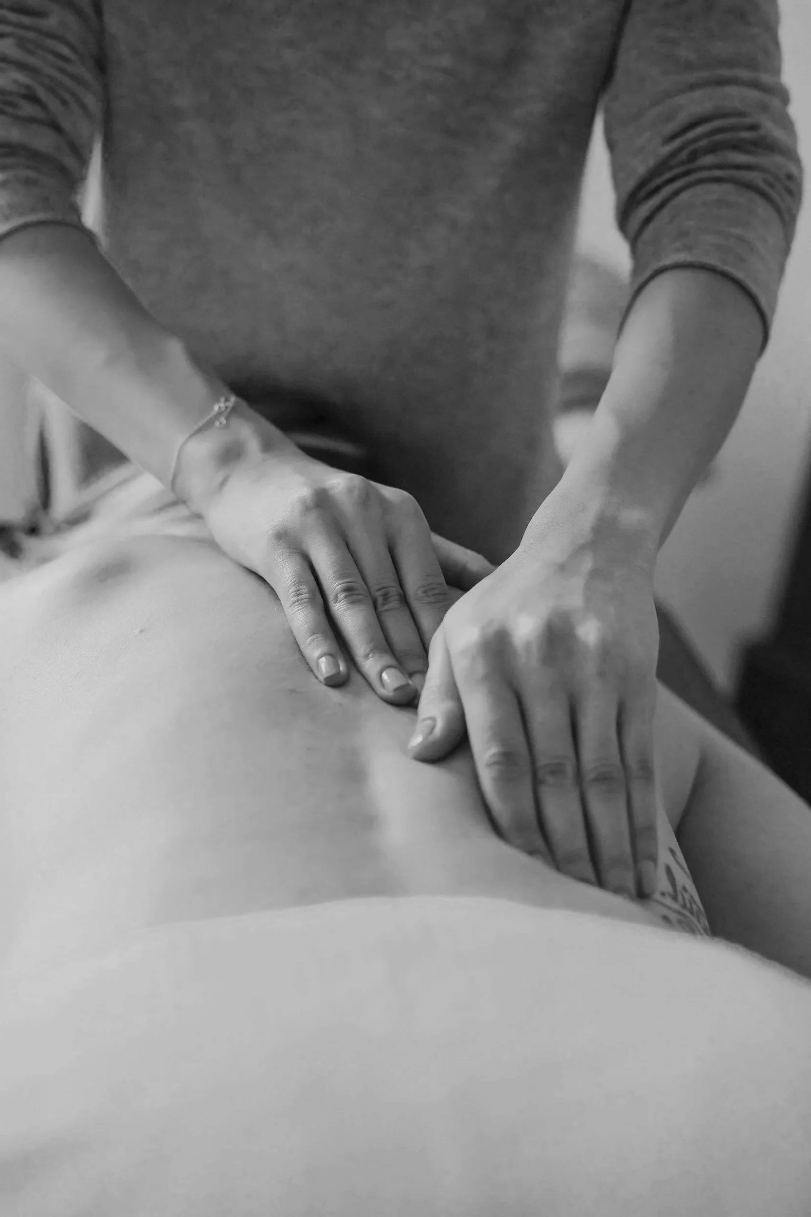 A person giving a massage to someone lying face down, with hands pressing on the back, in black and white.