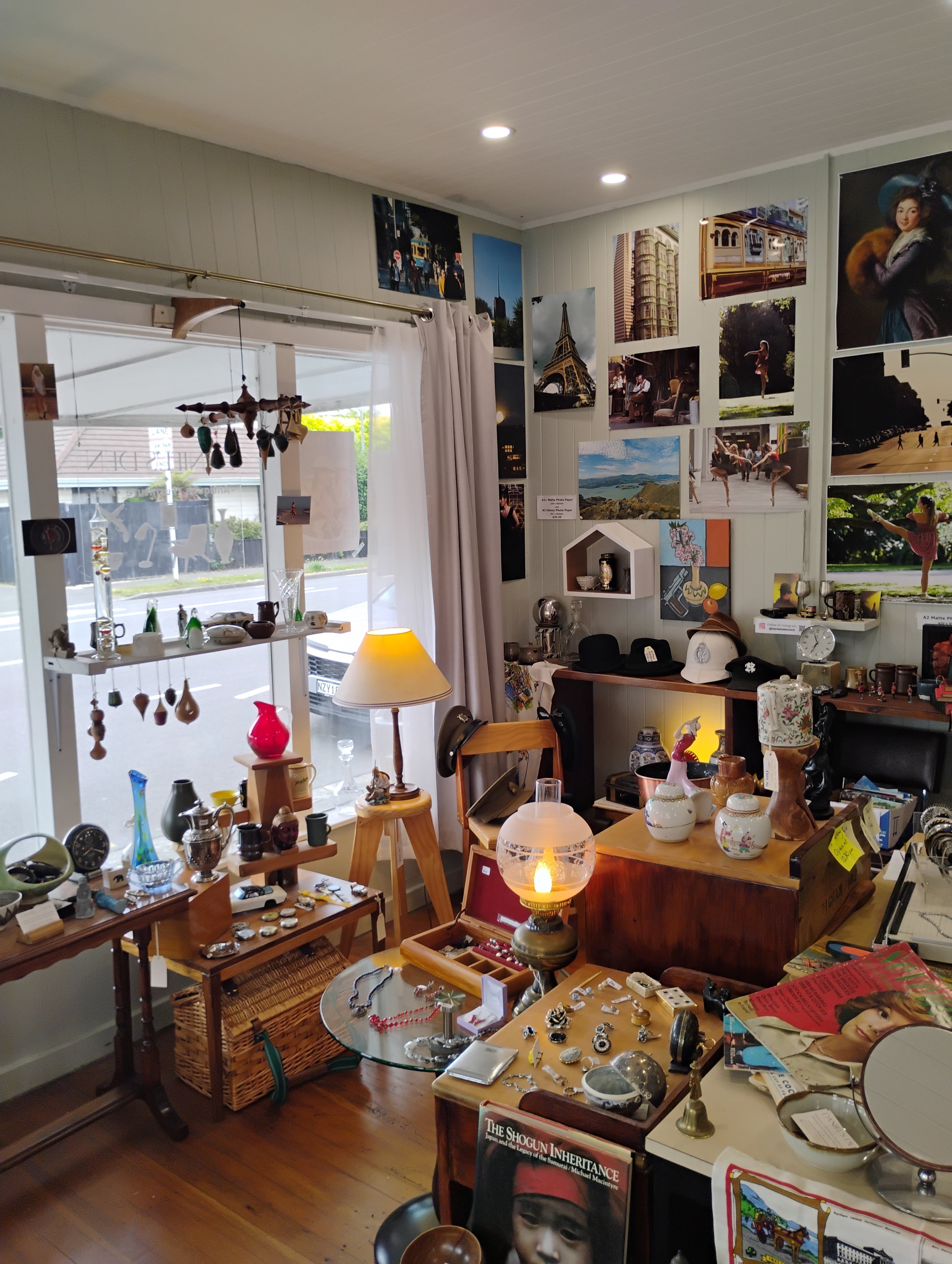 Interior of a thrift shop or antique store with various decorations, jewelry, pottery, framed photographs, and vintage items on tables and shelves, illuminated by natural and artificial light.