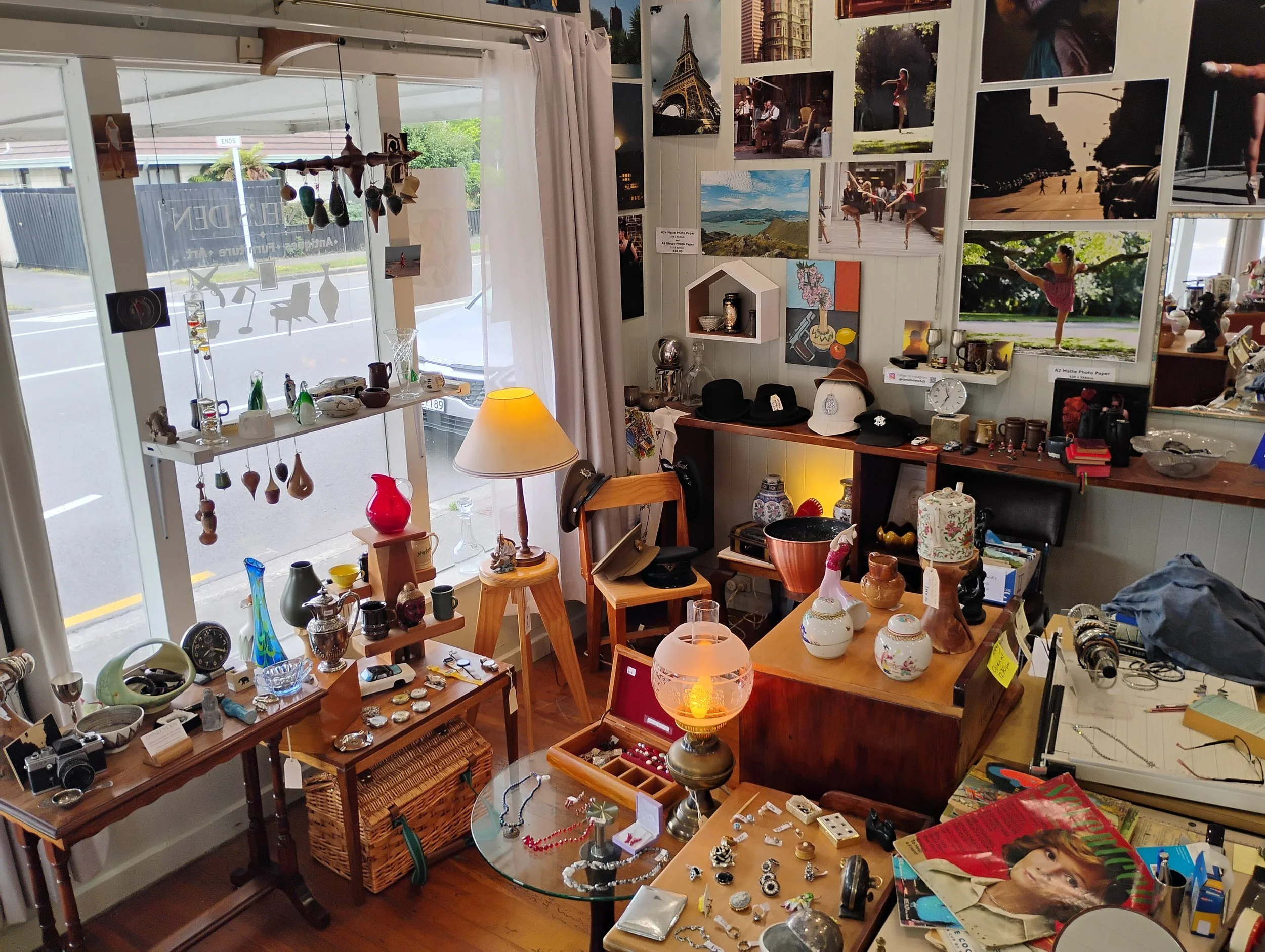 Interior of a thrift shop with various decorative items, including vases, jewelry, hats, cameras, and framed photos and posters on the walls. antique store chch.