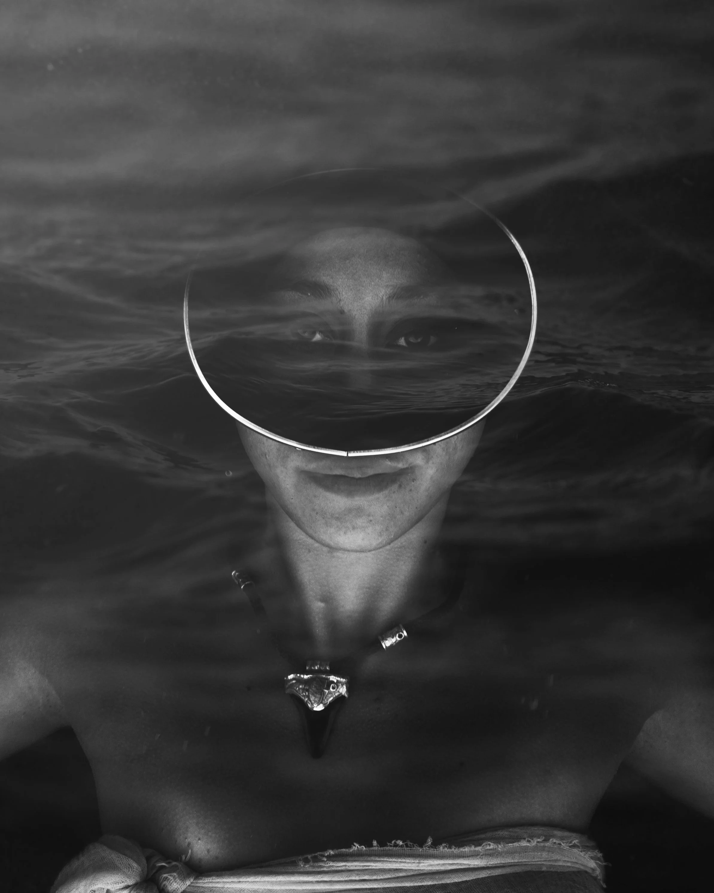 A person partially submerged in water, wearing goggles, with their face reflected in the water surface.