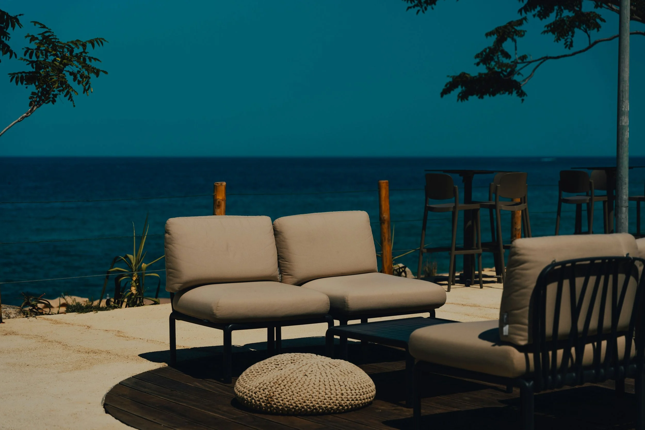 Salon de plage avec des fauteuils et un pouf, vue sur la mer.