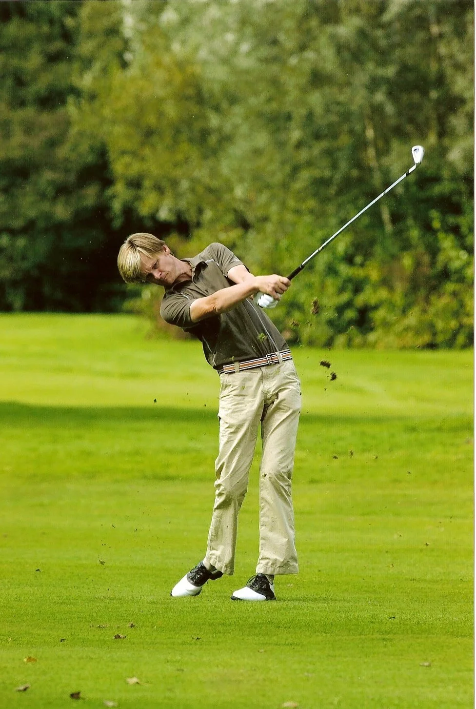 Man in een golfbaan slaat de golfbal met een golfclub, omgeving met gras en bomen.