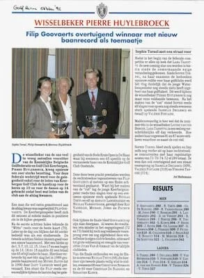 Twee mensen staan in een kamer met een man in een donkerblauw pak die een grote bokaal vasthoudt, tussen twee vrouwen. Ze lijken op een prijsuitreiking of ceremonie, met een koptekst over Wisselbekker Pierre Huylebroeck.