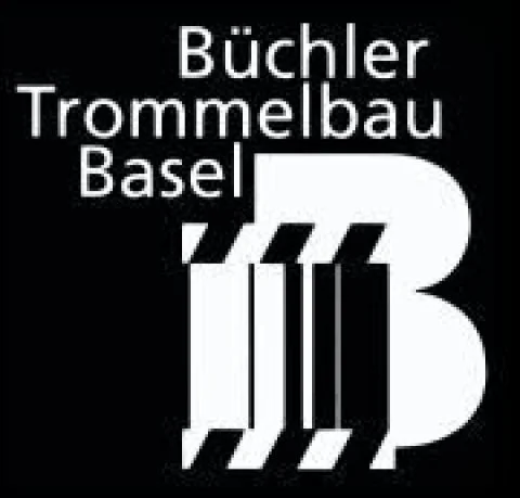 Schwarzes Hintergrundbild mit weißen Schriftzug "Büchler Trommelbau Basel" und einem stilisierten weißen Tuba- oder Trommel-Icon.