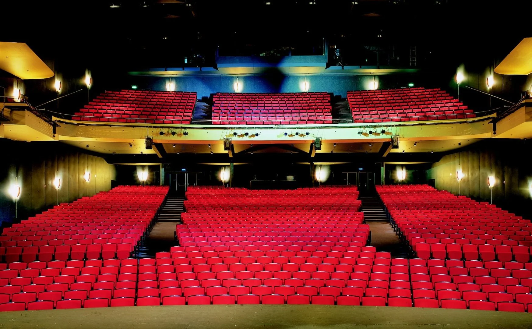 Leeres Theater mit roten Sitzen, beleuchtet und von dunklen Wänden umgeben.