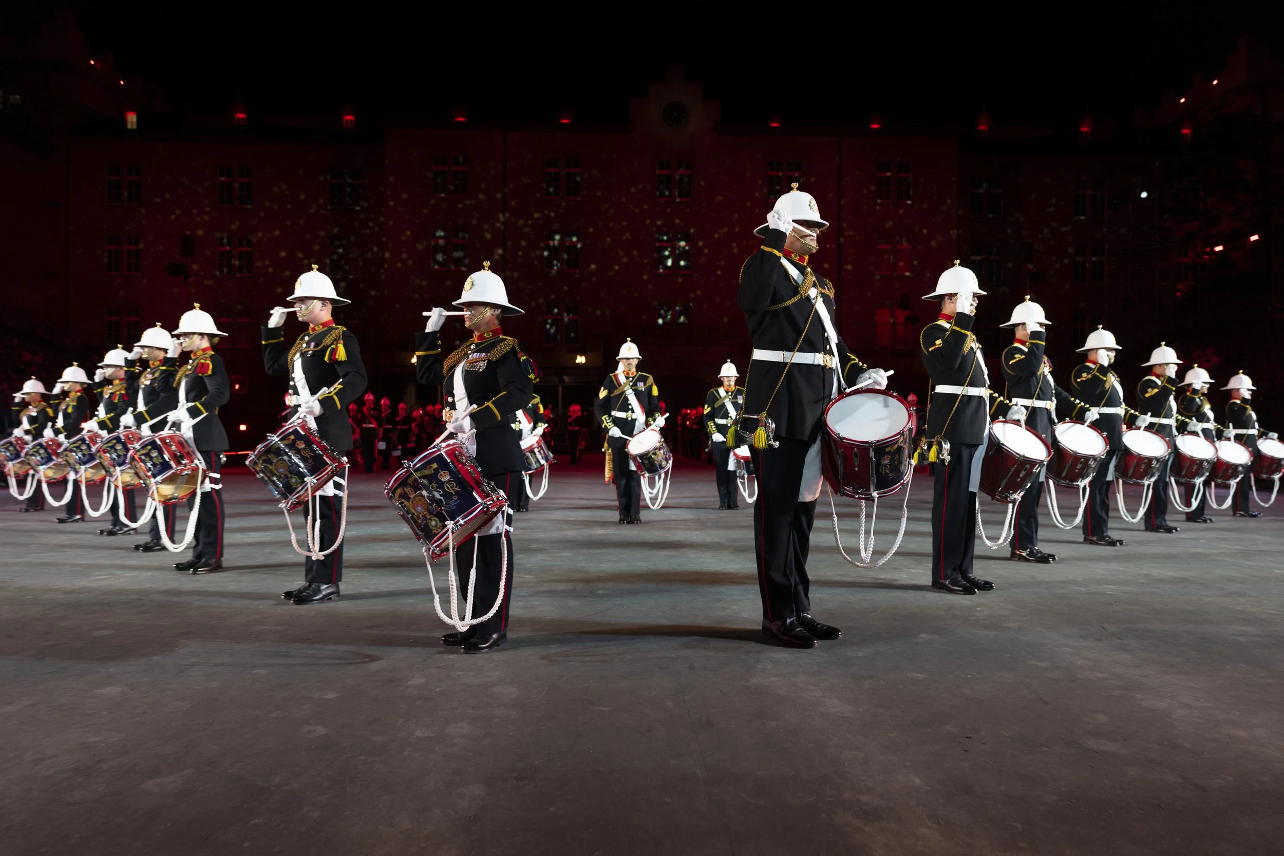 Marine Musikkorps bei einer Parade, die in Uniformen mit Helmen und Trommeln in einem Freiluftschauplatz aufgestellt sind.