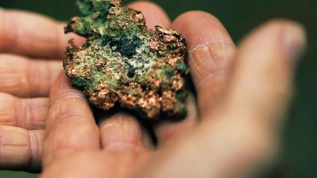 Close-up of a hand holding a piece of cannabis bud with green and orange hues.