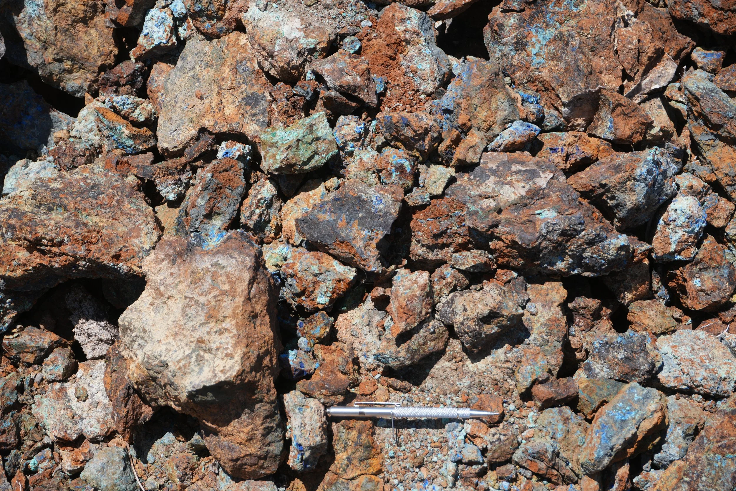 A pile of rust-colored rocks of various sizes with a metal pen lying among them.