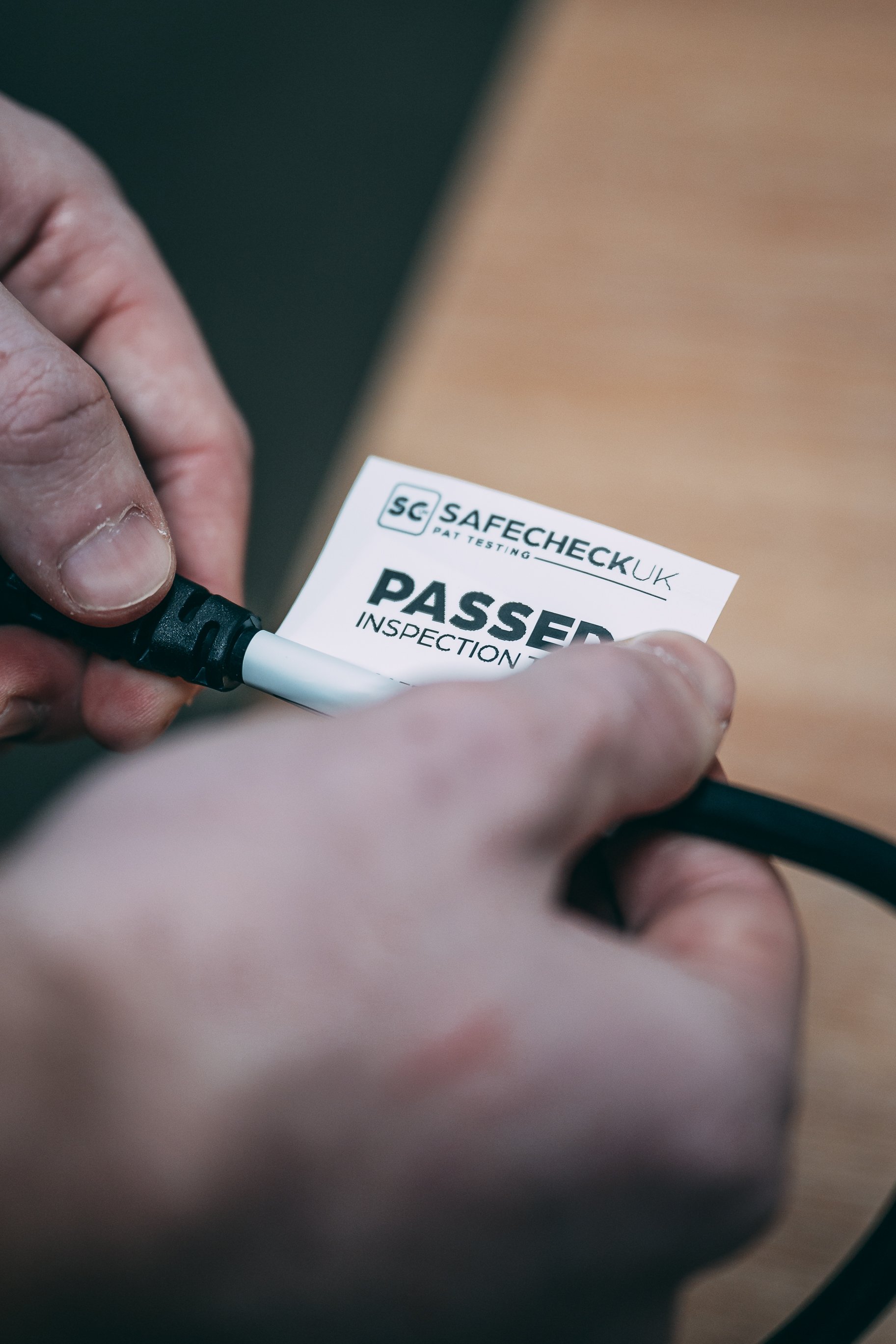 Close-up of a person holding and connecting an electrical power cord to a plug, with a sticker marked 'PASSED' indicating inspection approval.