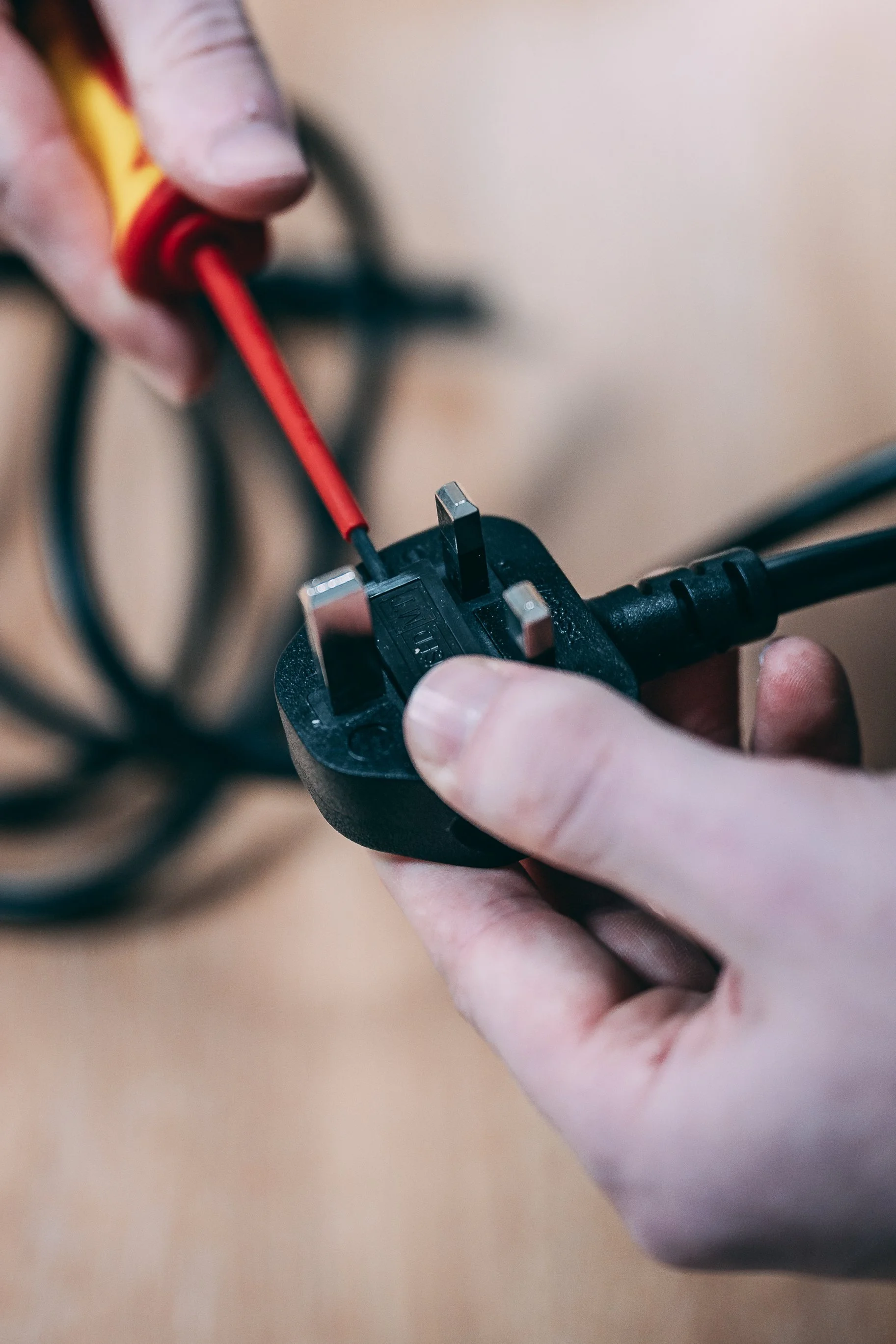Hands connecting an electrical plug to a power strip with a red and yellow screwdriver.
